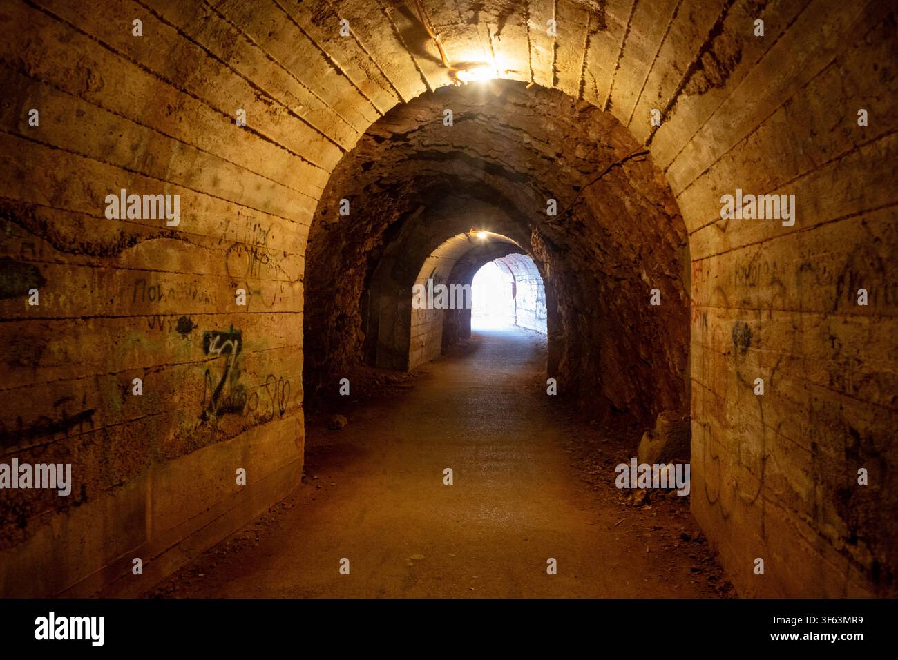 ein faszinierender unterirdischer Tunnel mit einem schwach beleuchteten Ende, aus Beton oder Stein gebaut, mit erdigen braunen und dunklen gelben Farbtönen, gesehen von der Stockfoto