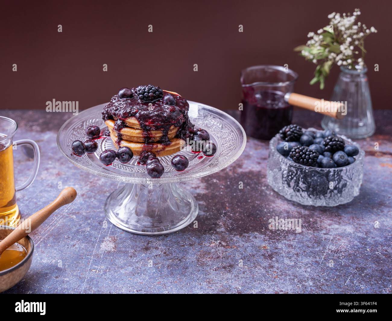 Hausgemachte Pfannkuchen, belegt mit Beerenkompott und frischen Blaubeeren, Brombeeren und Feigen, serviert auf einem eleganten Glaskuchenständer Stockfoto