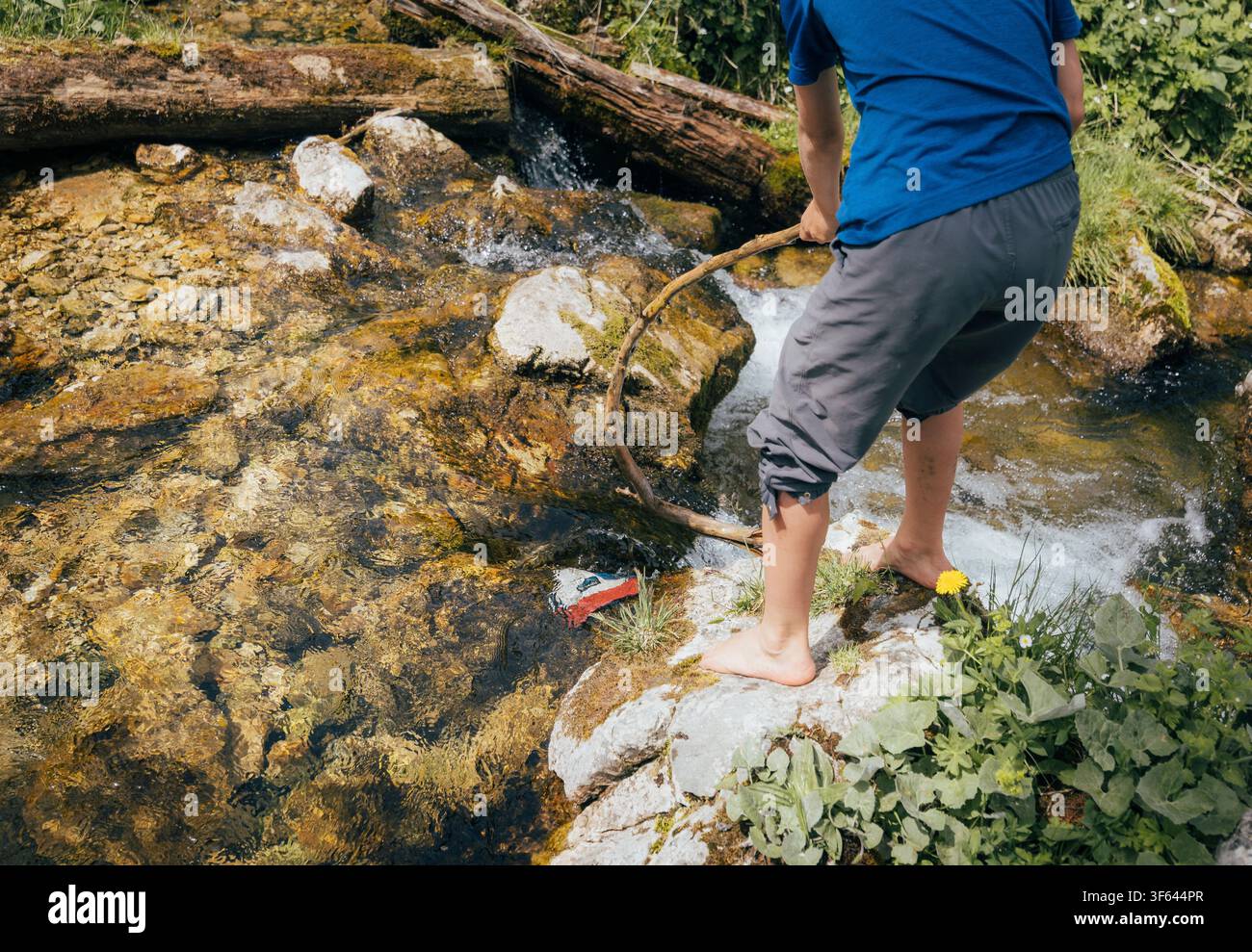 Ein Junge benutzt einen Stock, um nach seiner Baseballmütze zu greifen, während er in den Alpen wandert. Stockfoto