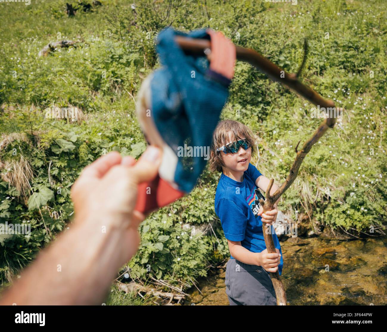 Ein Junge benutzt einen Stock, um nach seiner Baseballmütze zu greifen, während er in den Alpen wandert. Stockfoto