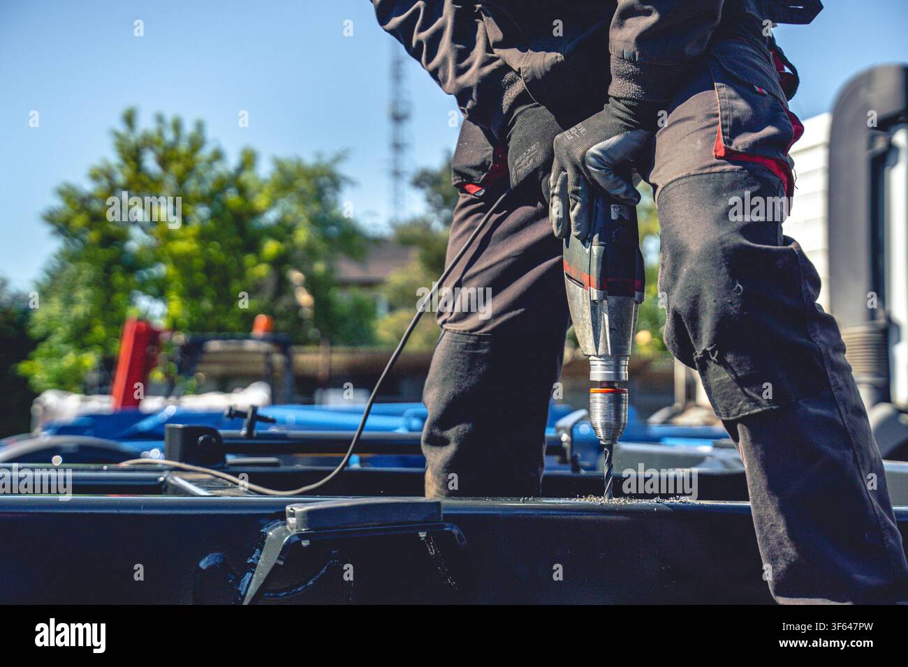 Nahaufnahme eines Arbeiters, der einen Akku-Bohrer verwendet, um ein Loch in einen schweren Metallstahlrahmen im Freien zu bohren, Konzept für Bau und Handarbeit Stockfoto