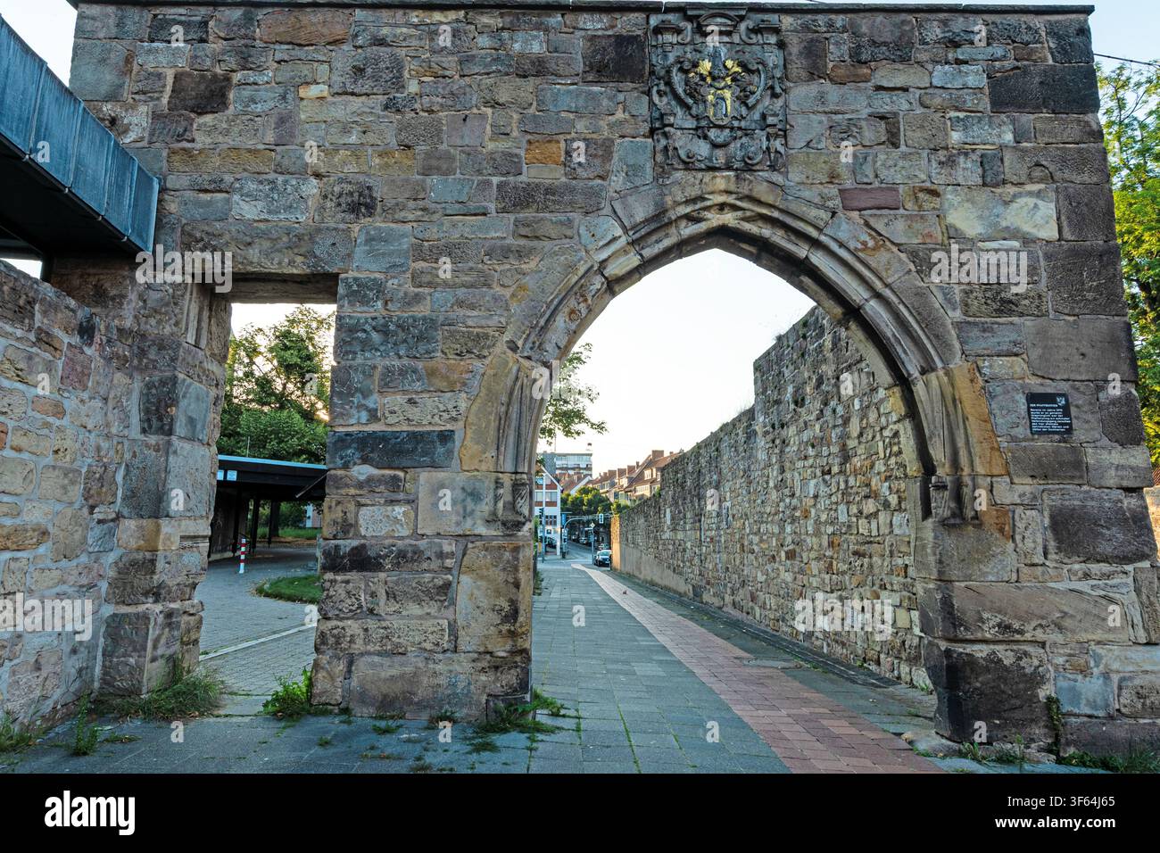 Historisches Steintor mit spitzem Bogen und heraldischem Wappen, das Teil einer alten befestigten Stadtmauer bildet. Stockfoto