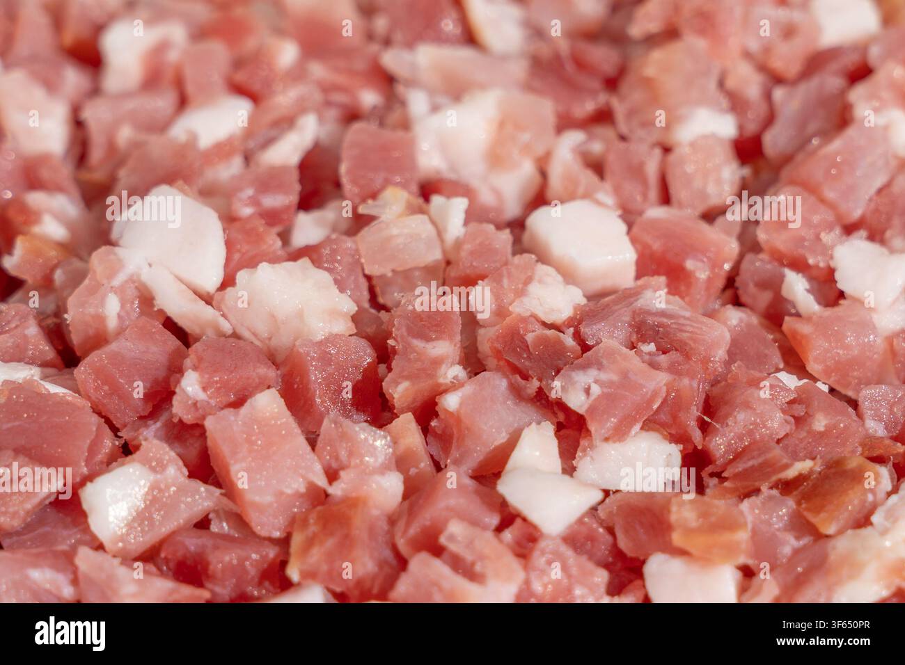 Fein gewürfelte rohe Schweinefleischstücke und Fettstücke füllen das gesamte Bild im Nahaufnahme. Das rosa magerte Fleisch und die weißen Fettwürfel zeigen eine frische, glänzende Textur, bereit Stockfoto