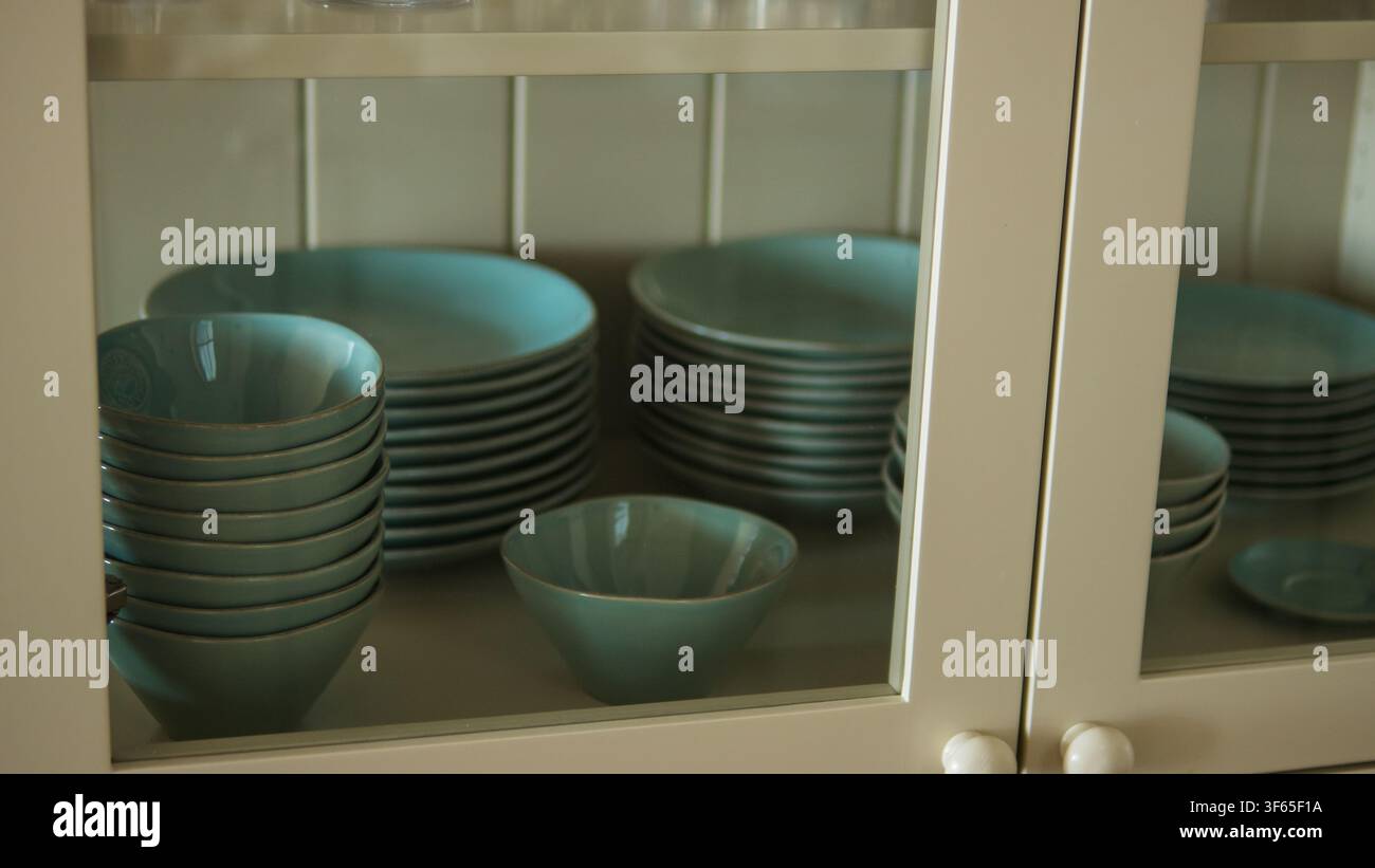 Stapel aus salbeigrünen Keramiktellern und -schüsseln hinter einer verglasten Schranktür in einer Landhausküchenkommode — Wohnraumgestaltung, ordentliche Aufbewahrung Stockfoto