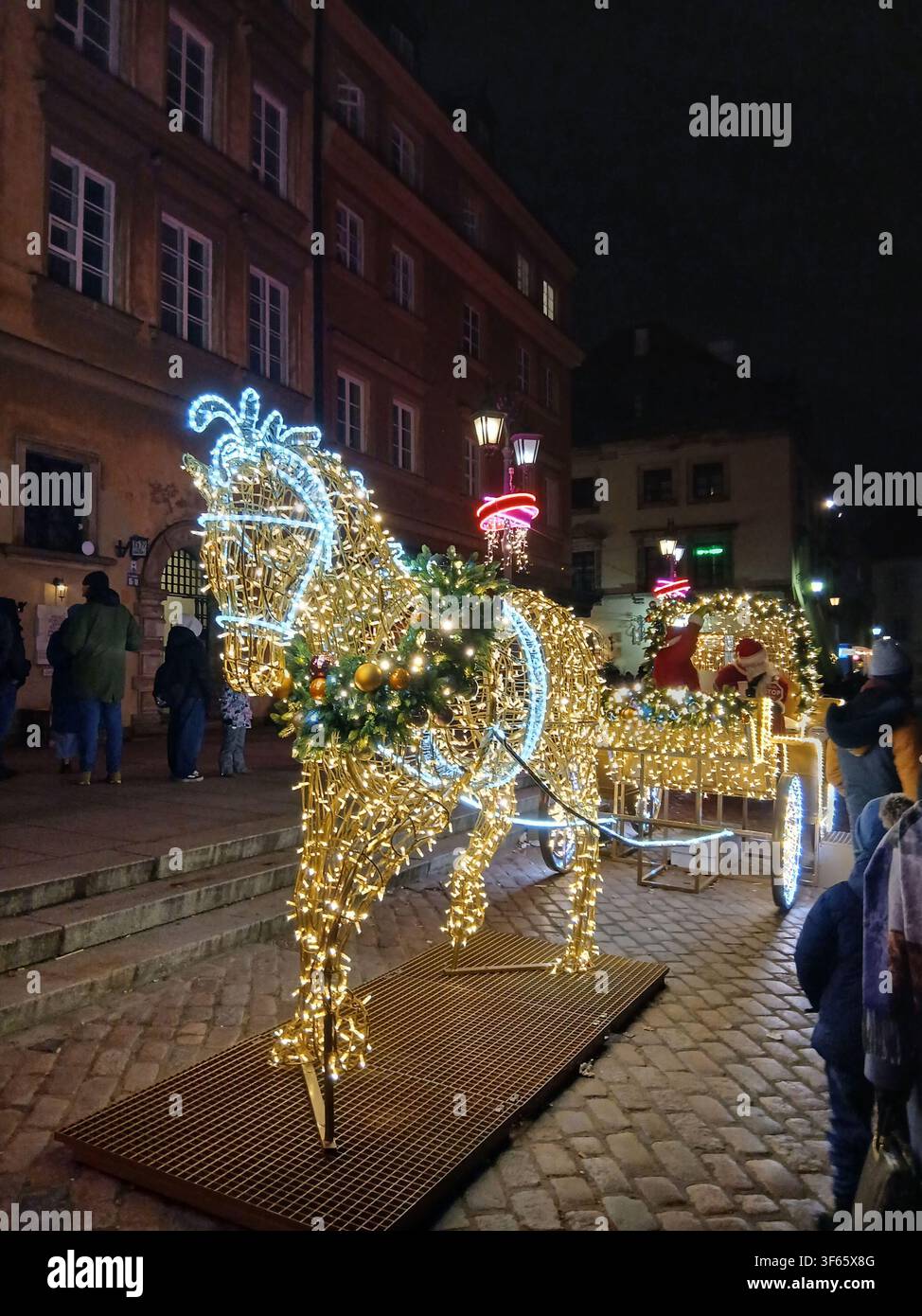 Festliche Weihnachtsbeleuchtung einer leuchtenden Pferde- und Kutschenskulptur auf einer europäischen Stadtstraße bei Nacht, Feiertagslichtinstallation. - Smartphone-aufgenommenes Stockfoto