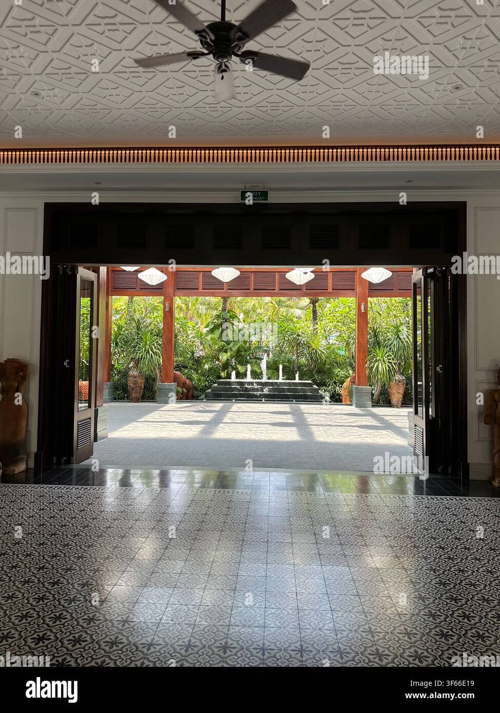 Resort-Lobby-Tür mit Blick auf den tropischen Innenhof. Blick von einer eleganten Hotel-Lobby im Innenbereich mit gemustertem Fliesenboden durch eine offene Tür - Smartphone-aufgenommenes Stockfoto
