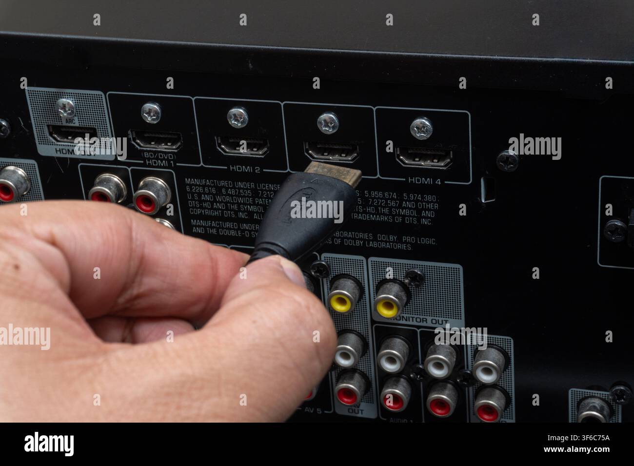 Hand steckt HDMI-Kabel in AV-Receiver. Nahaufnahme zeigt Anschlüsse und Verbindungsdetails. Nützlich für Technik-, Setup- oder Reparaturinhalte Stockfoto