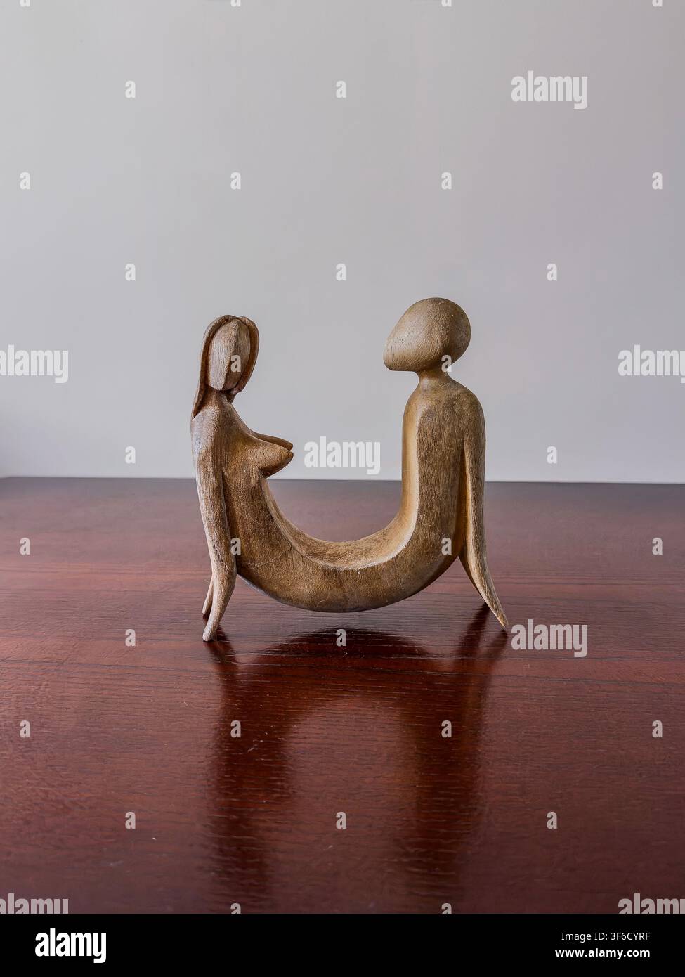 Stilisierte Skulptur zweier abstrakter menschlicher Figuren, die sich gegenüber sitzen auf einer Holzoberfläche vor einem schlichten Hintergrund. - Smartphone-aufgenommenes Stockfoto