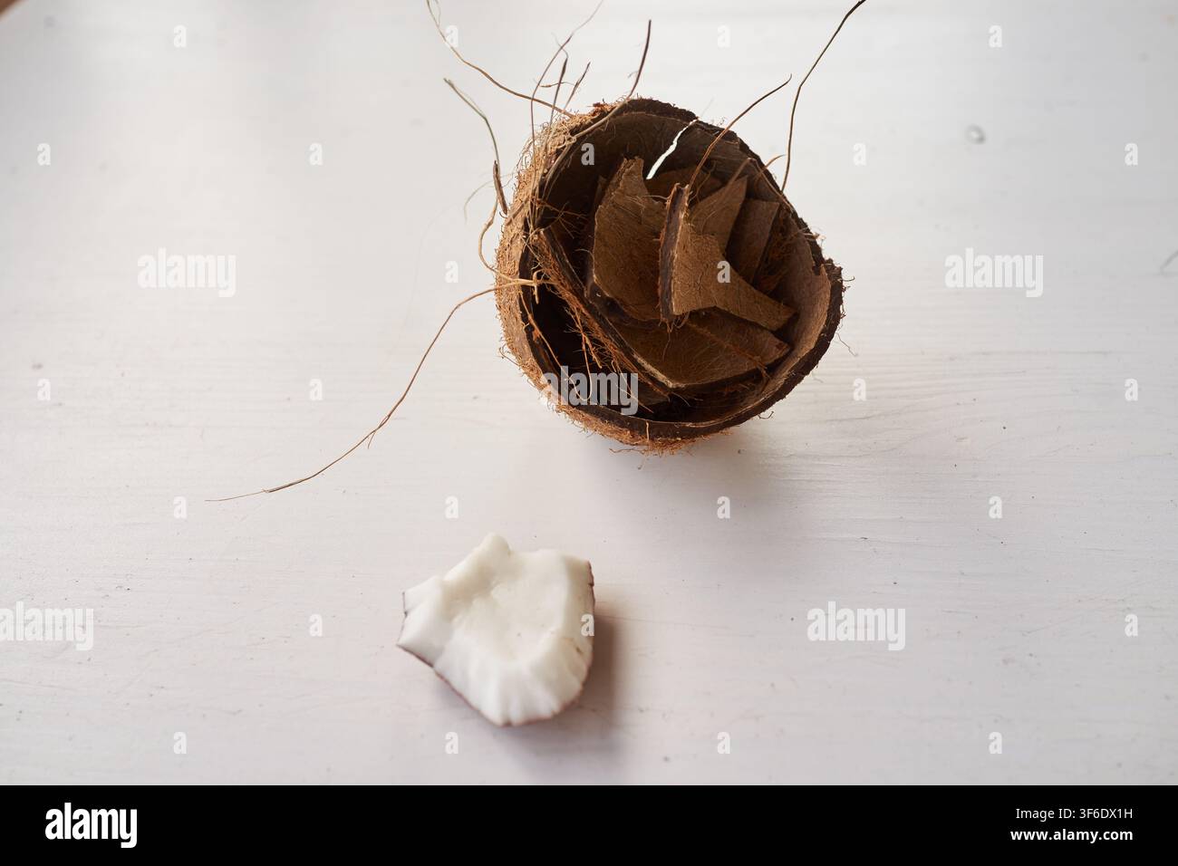 Kokosnuss-Schale liegt neben frischem weißem Fleisch. Weiße Oberfläche hält beide Hälften mit natürlicher Textur. Das Kokosnuss-Fleisch wirkt weich und unberührt. Bild schlägt vor Stockfoto