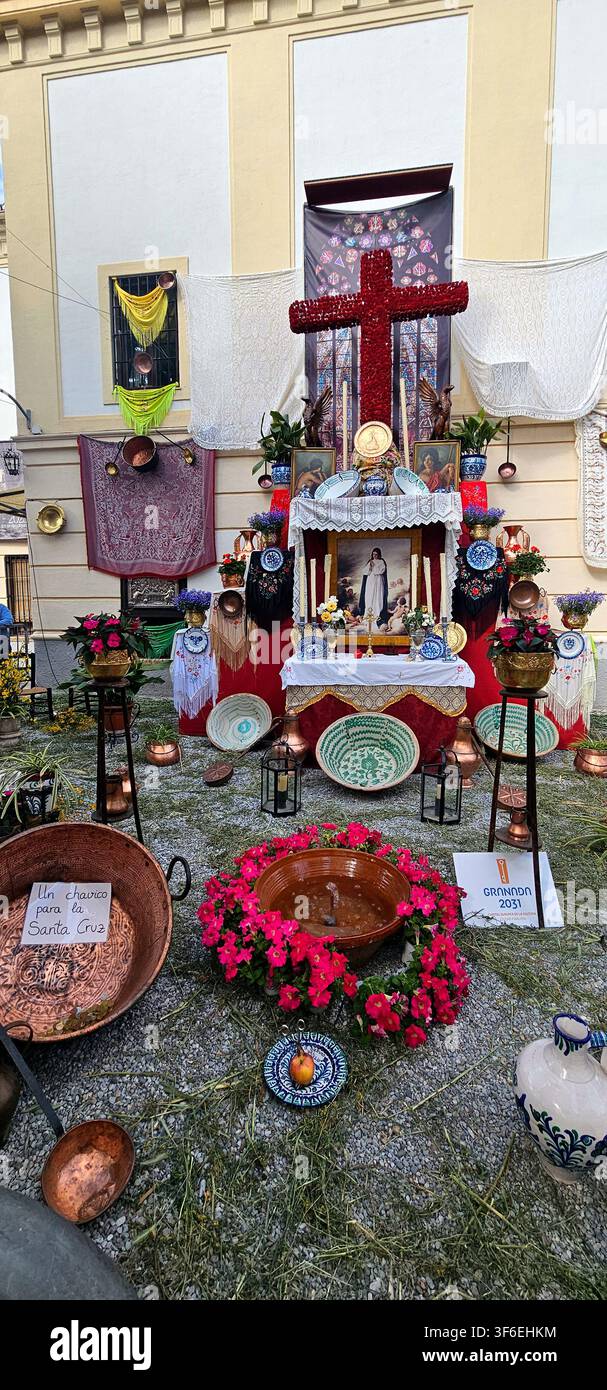Rotes Blumenkruzifix, das auf einem geschmückten Freialtar mit Keramikschalen, Blumen, Textilien und religiösen Bildern während des Cruces de Mayo-Fests ausgestellt ist. Stockfoto