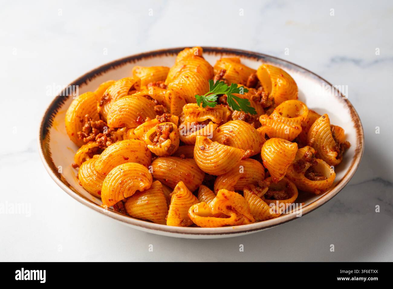 Köstliche Pipe Rigate Pasta mit Bolognese-Fleischsauce und frischen Basilikumblättern Stockfoto