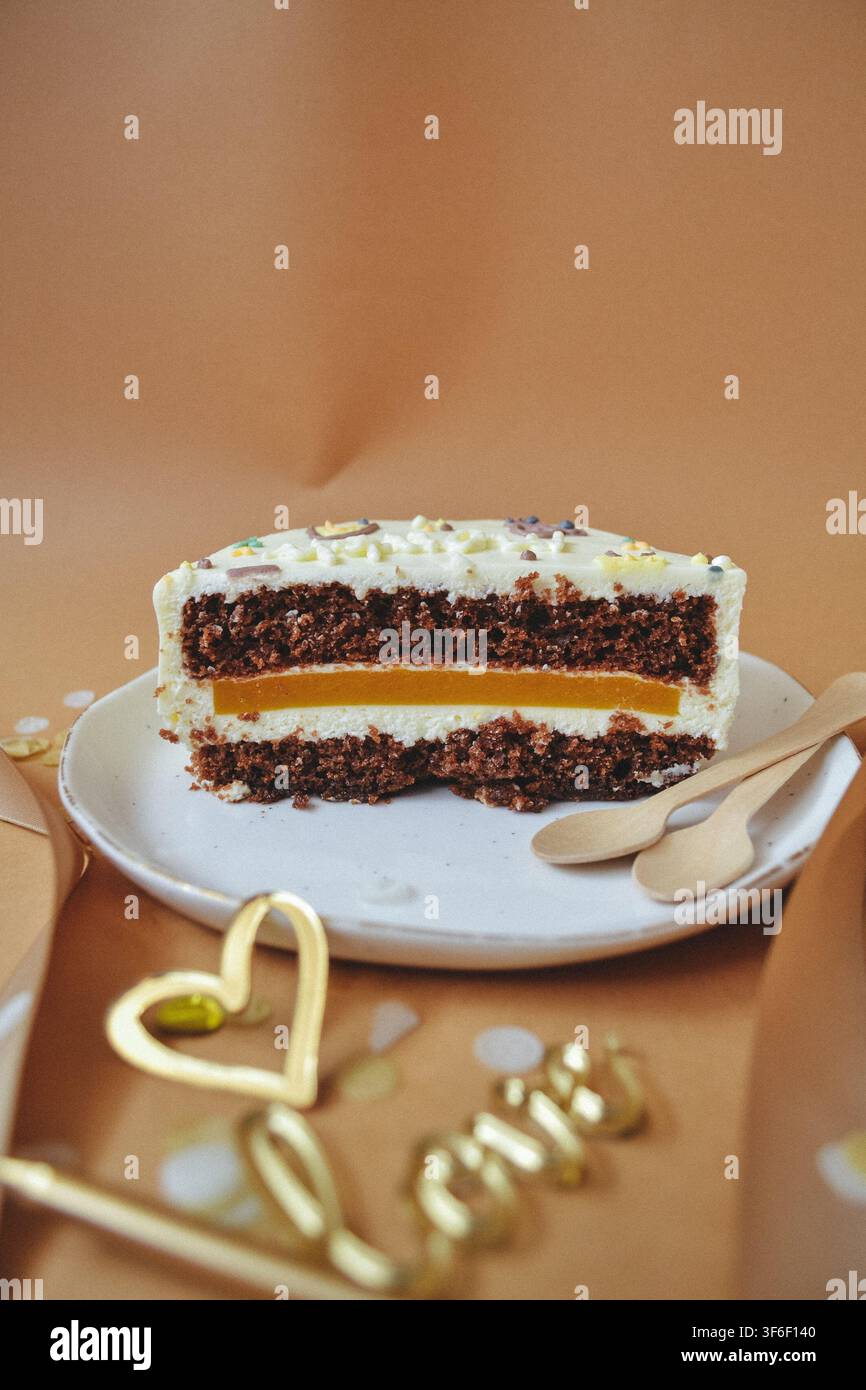 Scheibe Schokoladenspongekuchen mit Mangogelée-Schicht und weißer Sahne auf beigem Hintergrund, romantisches Urlaubskonzept Stockfoto