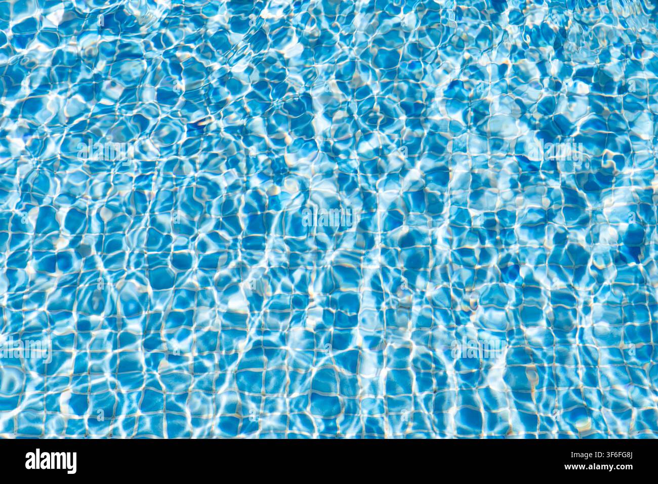 Das Sonnenlicht bricht sich im klaren blauen Wasser und erzeugt schimmernde Muster auf der gefliesten Oberfläche eines Schwimmbeckens Stockfoto