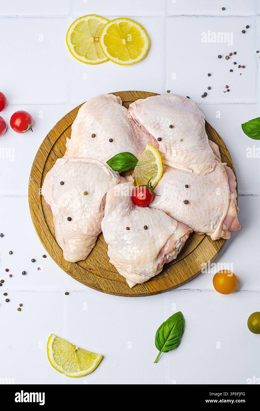 Rohe Hähnchenschenkel mit Gemüse auf einem Holzbrett, auf weißem Hintergrund. Stockfoto