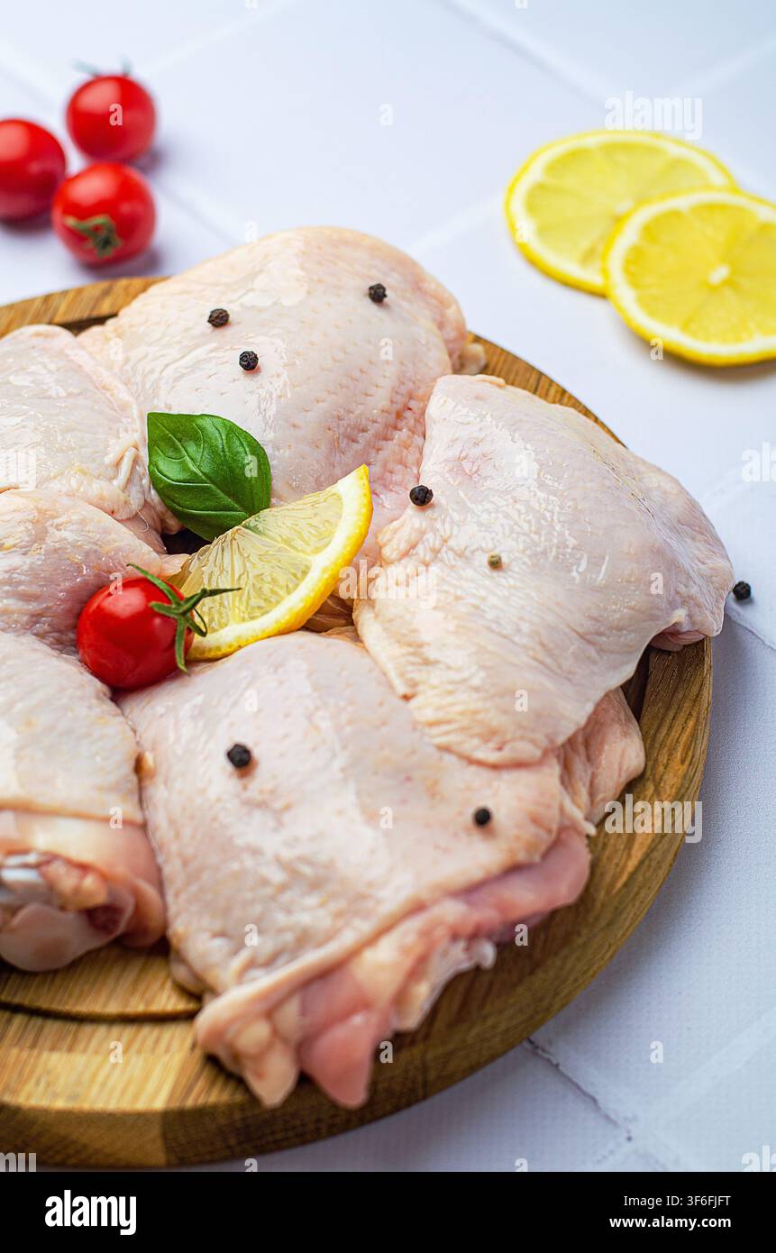 Rohe Hähnchenschenkel mit Gemüse auf einem Holzbrett, auf weißem Hintergrund. Stockfoto