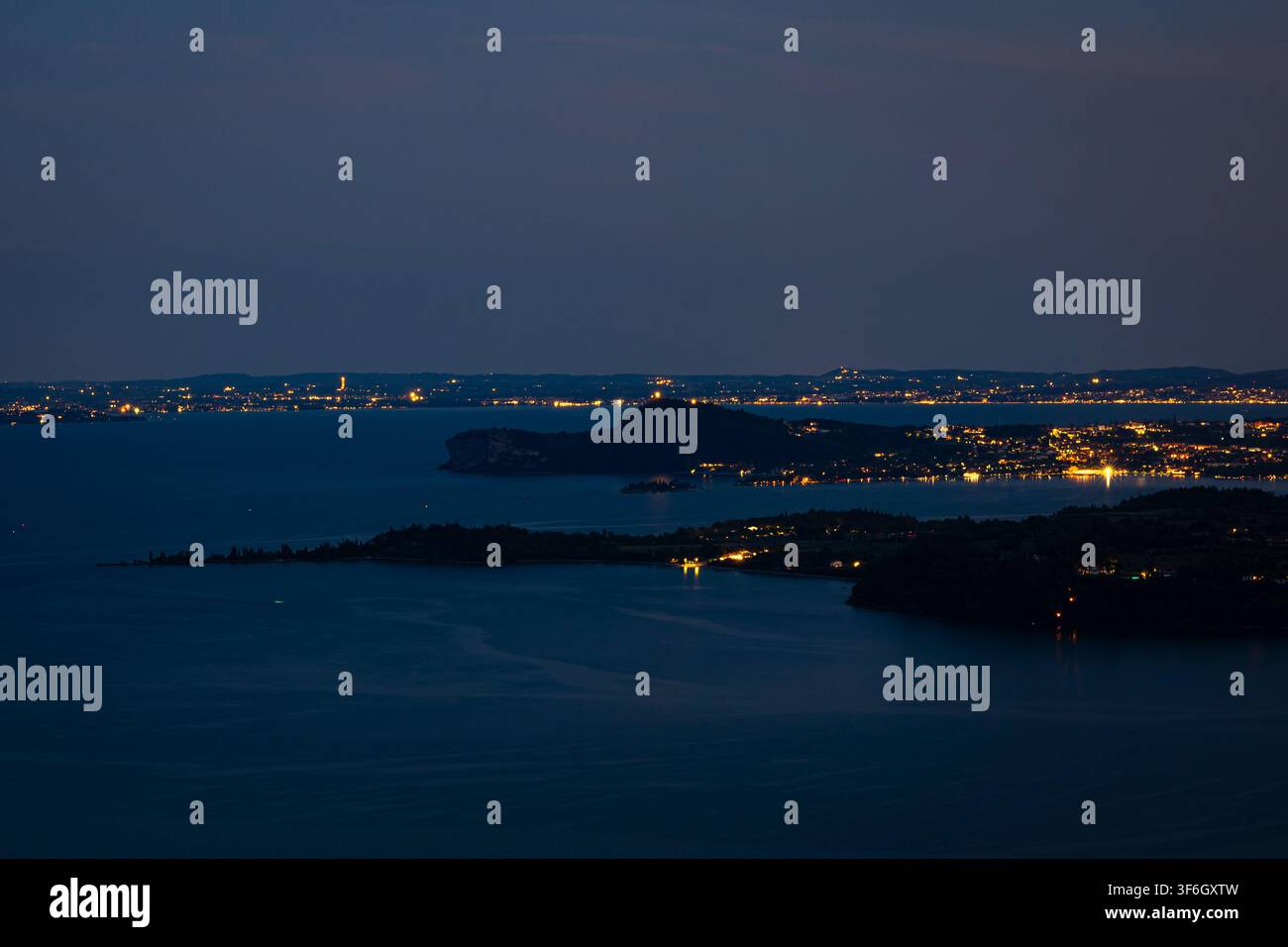 Küsten-Nachtpanorama mit Silhouetteninseln und fernen Stadtlichtern am Gardasee, Italien in der Dämmerung Stockfoto