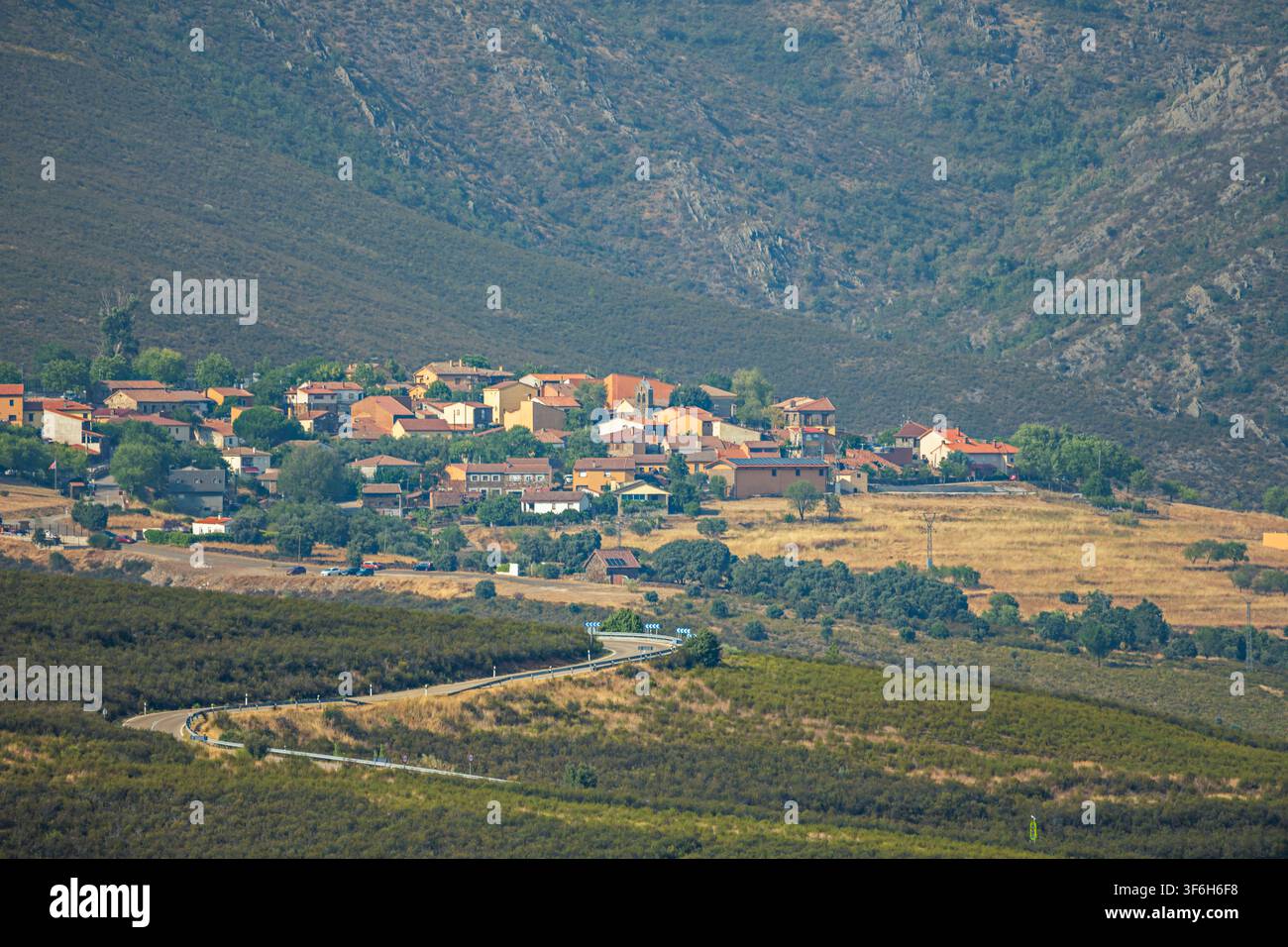 Traditionelles Steindorf mit Terracotta-Dächern liegt unterhalb eines schroffen Berghangs, eine kurvenreiche Straße führt durch die Landschaft Stockfoto
