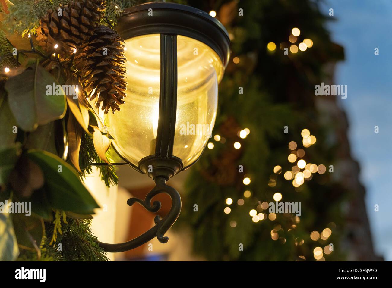Festliche Grünpflanzen und warme Weihnachtslichter schmücken eine klassische Straßenlaterne in Kensington, London, um die Feiertagssaison zu feiern. Stockfoto