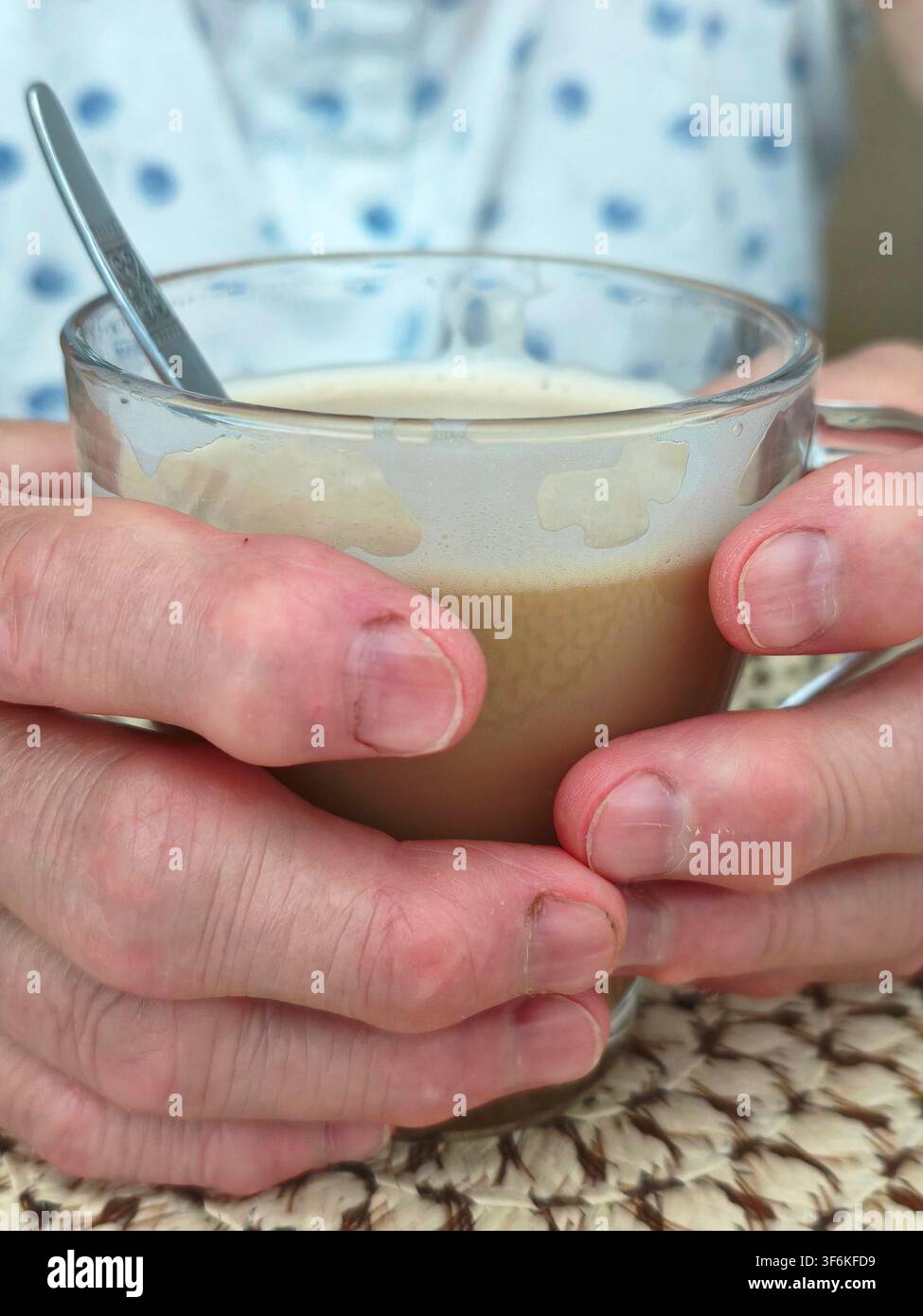 Ältere Person hält eine warme Glas Tasse Kaffee mit Milch während einer Morgenroutine zu Hause Stockfoto