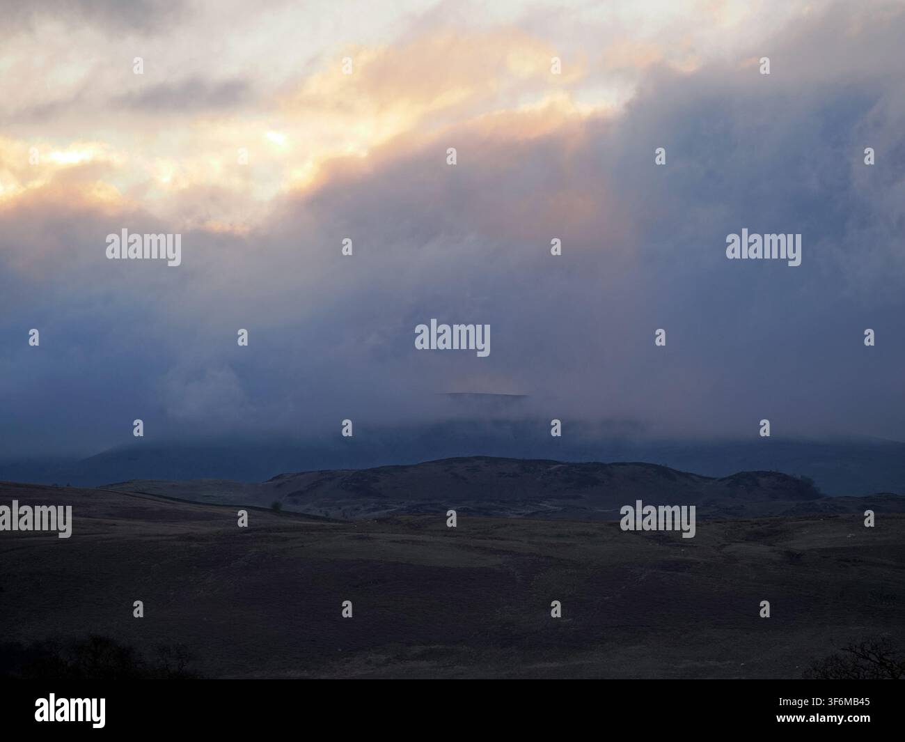 dramatisches, im Turner-Stil gemaltes Abendlicht über düsteren Lakeland-Fells mit einem Blick auf die ferne Skyline durch eine Lücke in den Wolken Cumbria, England, UK Stockfoto