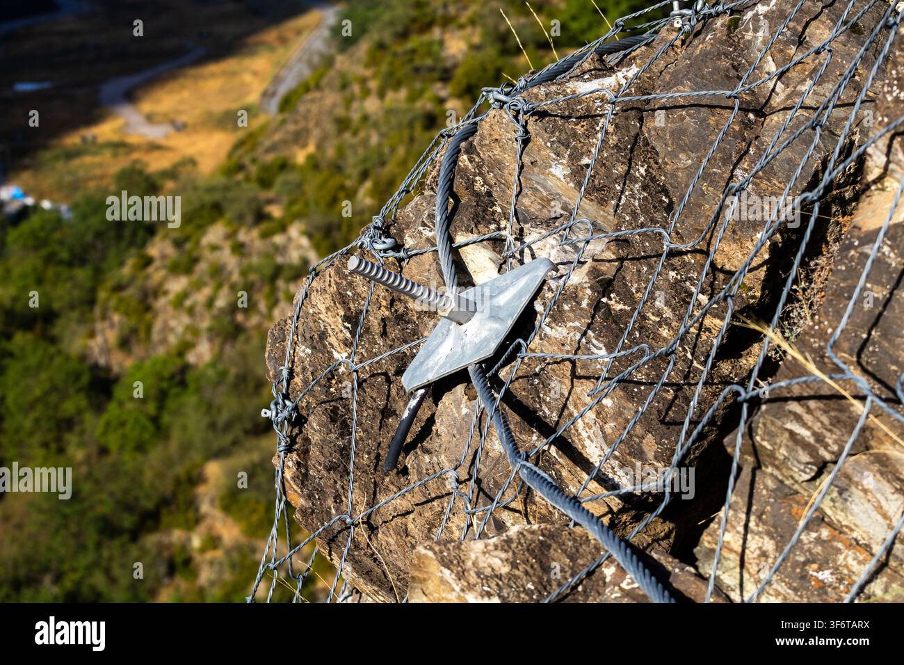 Nahaufnahme eines Stahl Drahtgitters und Verankerungssystems, das auf einem felsigen Hang installiert wurde, um Steinschläge zu verhindern und instabiles Gelände zu stabilisieren. Dieses geotechnische e Stockfoto