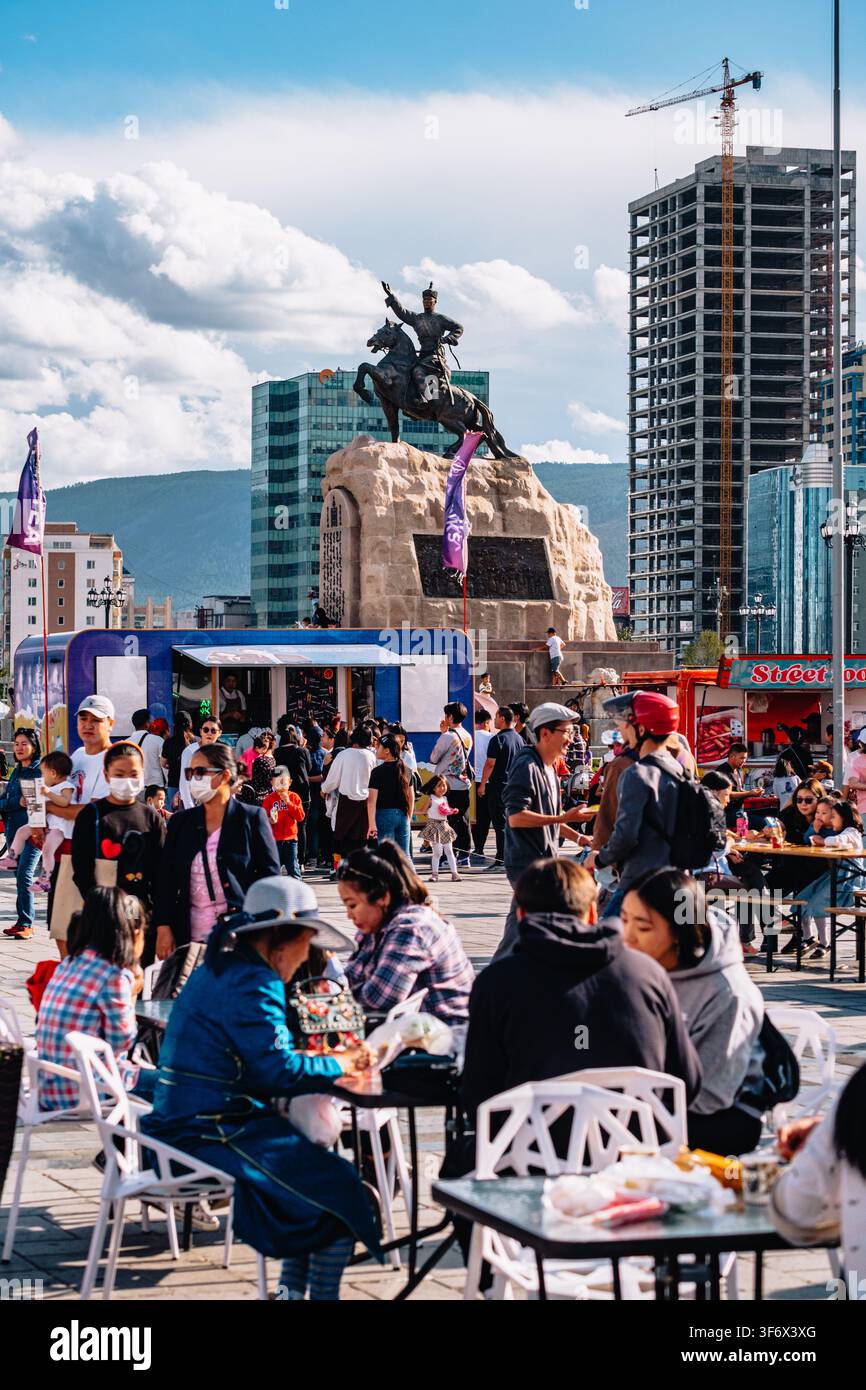 Menschenmassen genießen das UB Food Festival am Sukhbaatar-Platz in Ulaanbaatar mit dem Damdin Sukhbaatar-Denkmal im Hintergrund. Stockfoto