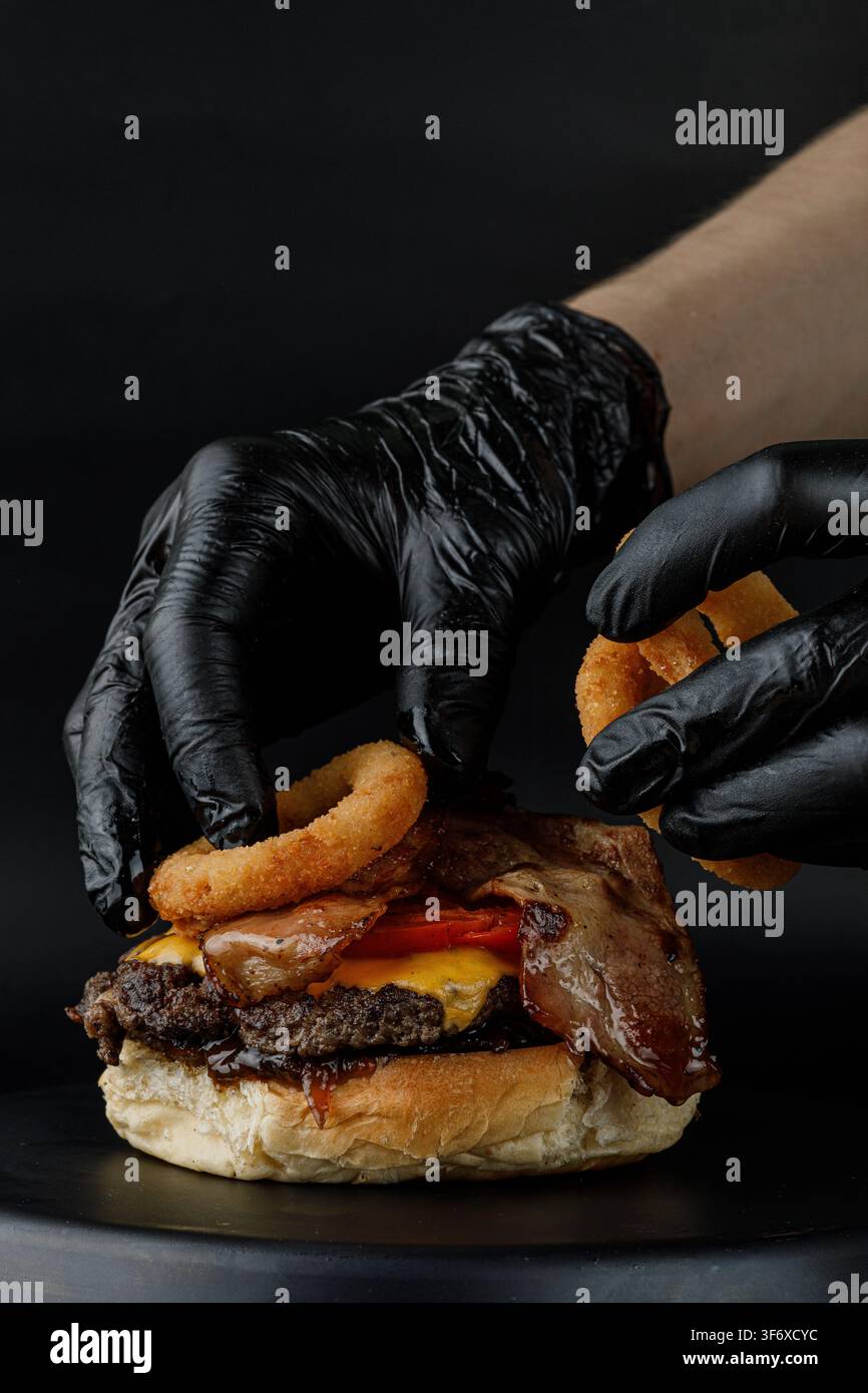 Chef fügt knusprige Zwiebelringe zu einem Gourmet-Burger hinzu Stockfoto
