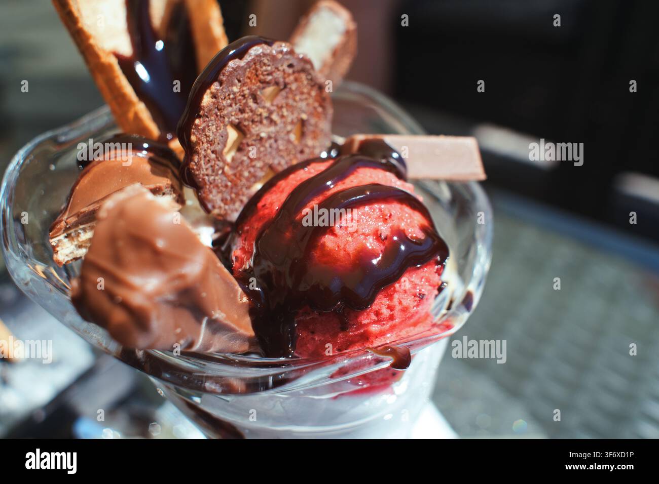 Nahaufnahme eines köstlichen Eisbechers, der in einer Glasschale serviert wird, reichlich mit Schokoladensirup, knusprigen Waffeln, Keksen und Schokoladenstücken belegt. Stockfoto