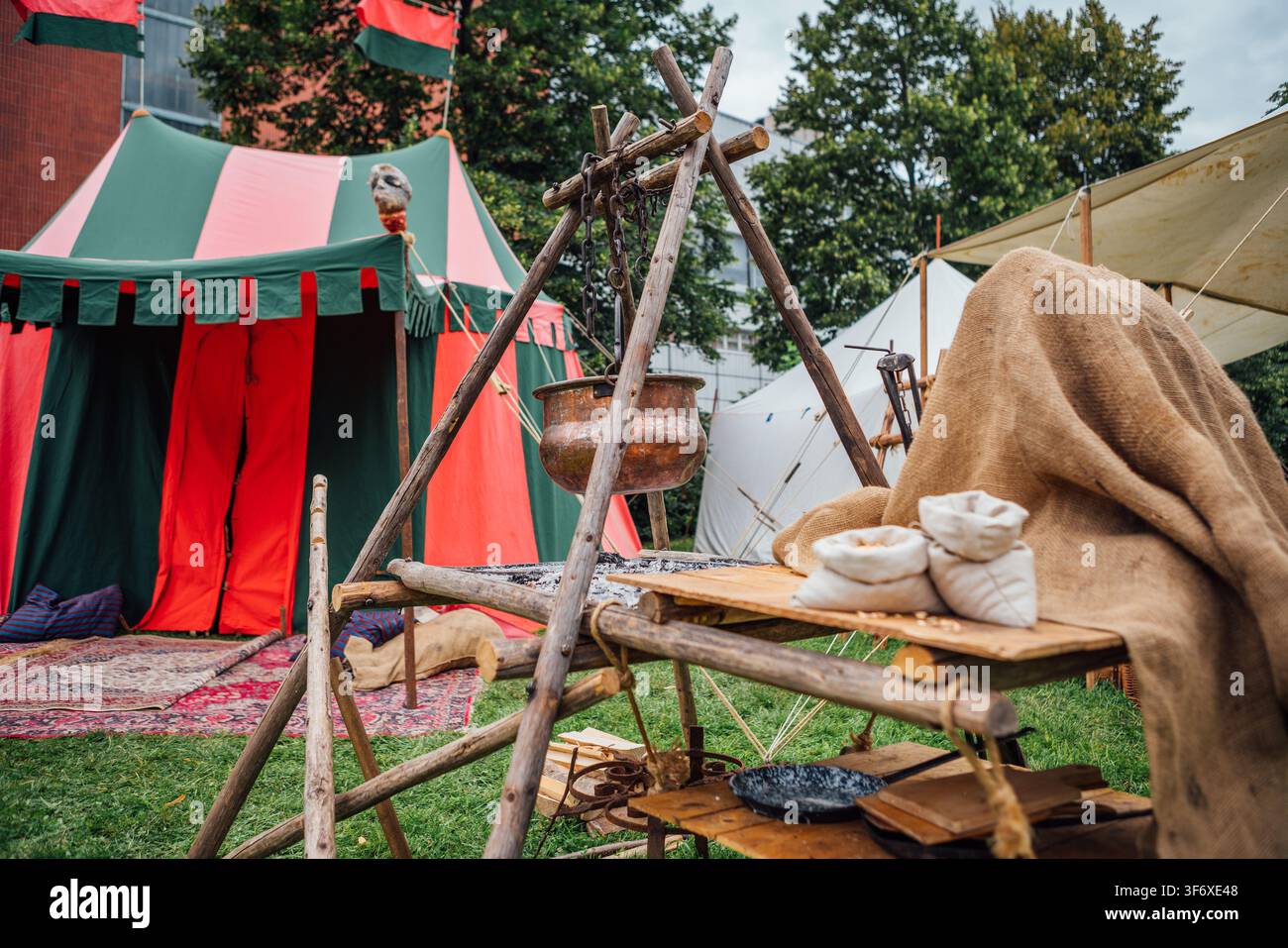Mittelalterliches Festival-Lager mit farbenfrohem Zelt, offenem Feuerplatz und Holztischaufbau – historischer Nachbau im Freien Stockfoto