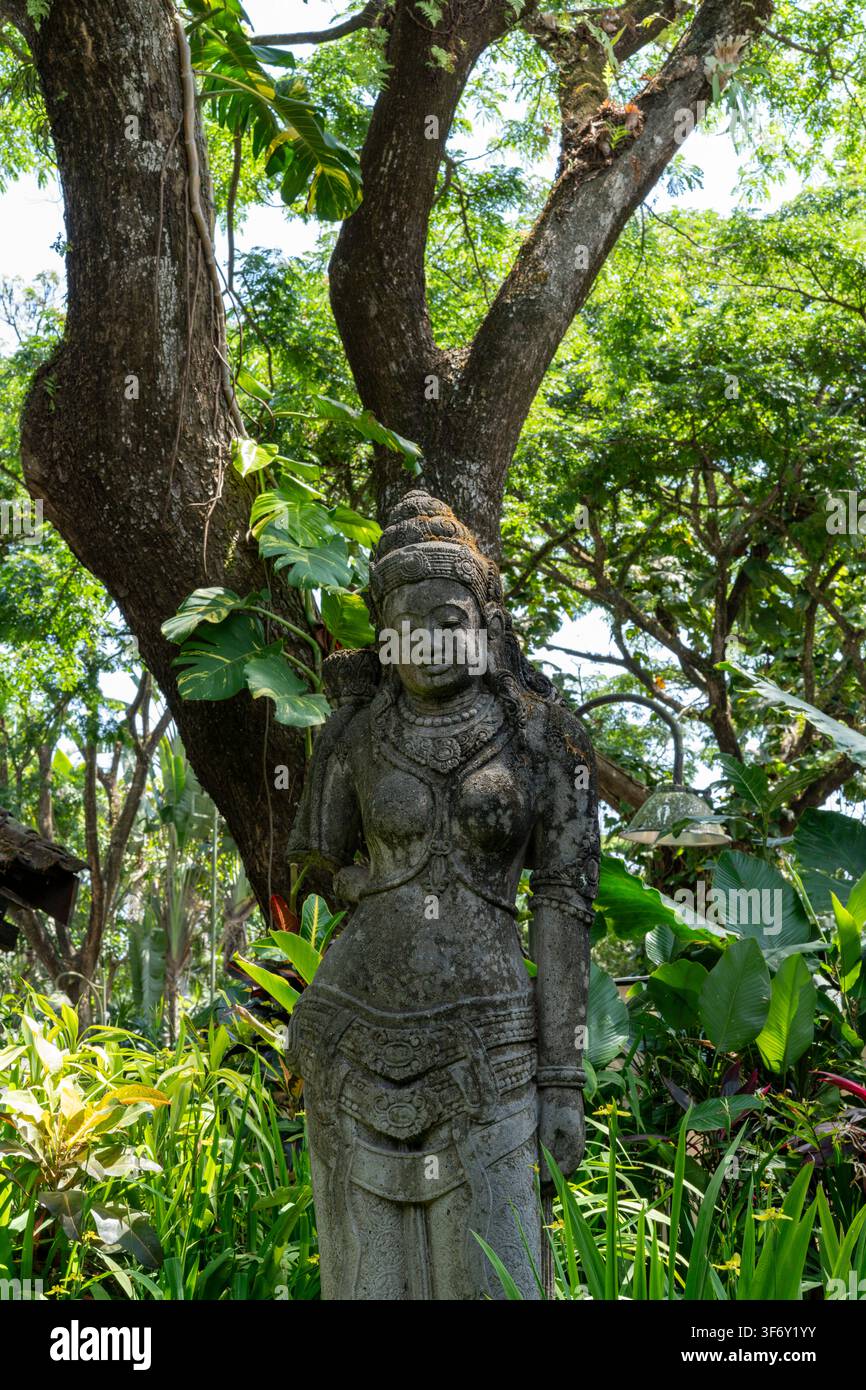 Eine traditionelle javanische Steinstatue einer weiblichen Gottheit unter einem großen Baum in einem tropischen Garten in Kota Araya, Malang, Ostjava, Indonesien. Stockfoto