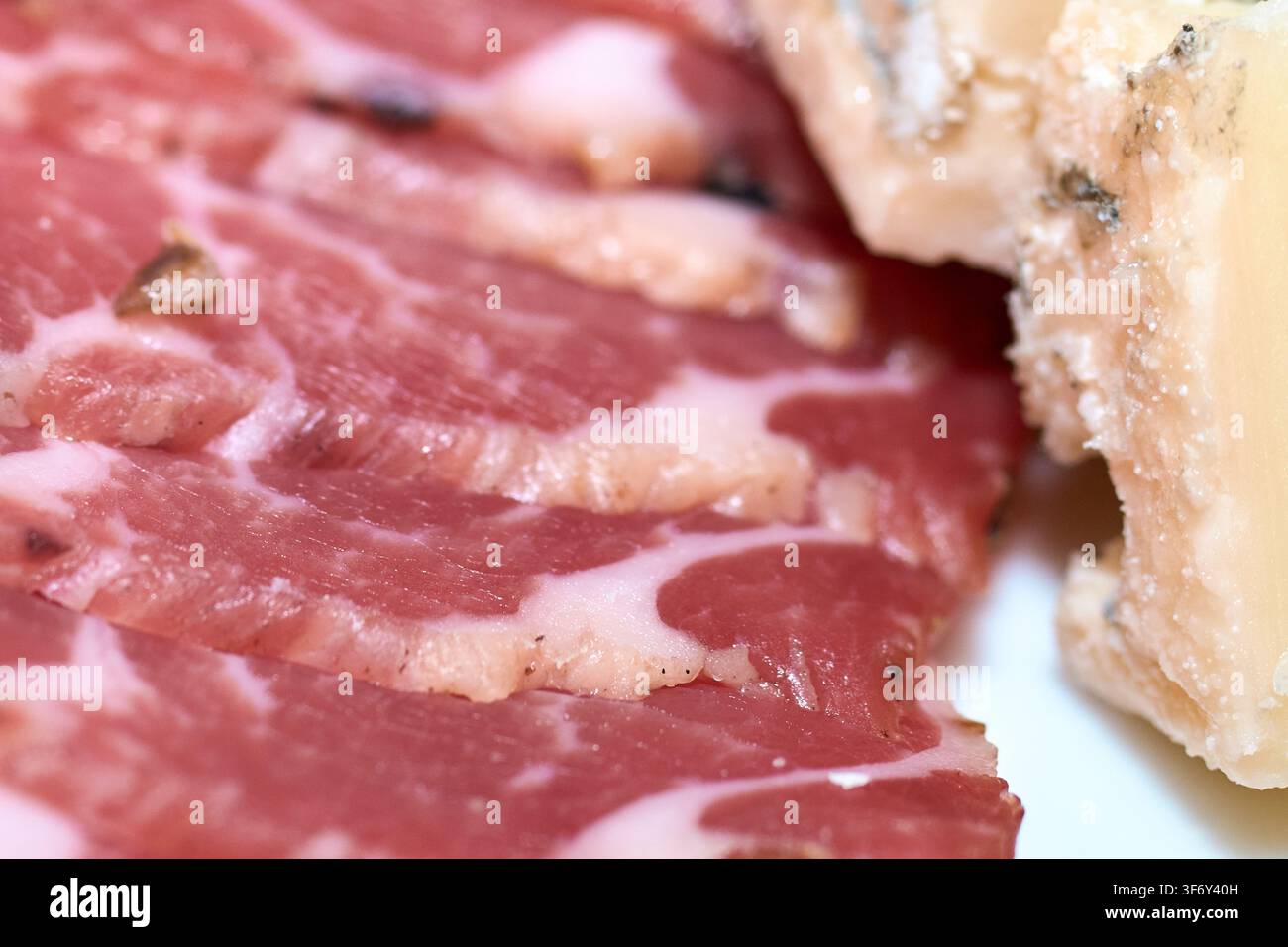 Nahaufnahme von fein filetiertem Schink mit marmorierter Struktur neben einem Stück gealtertem Käse, das die Zubereitung von Gourmetkost hervorhebt. Stockfoto