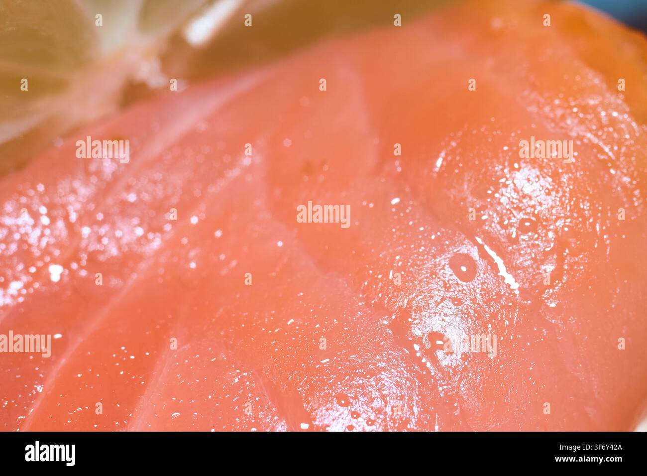 Extrem Nahaufnahme eines reichhaltigen rauchigen Lachsfiletschnitts, garniert mit einer frischen Limettenscheibe, die das weiche, rot strukturierte Fleisch und die glitzernden Öle zeigt. Stockfoto