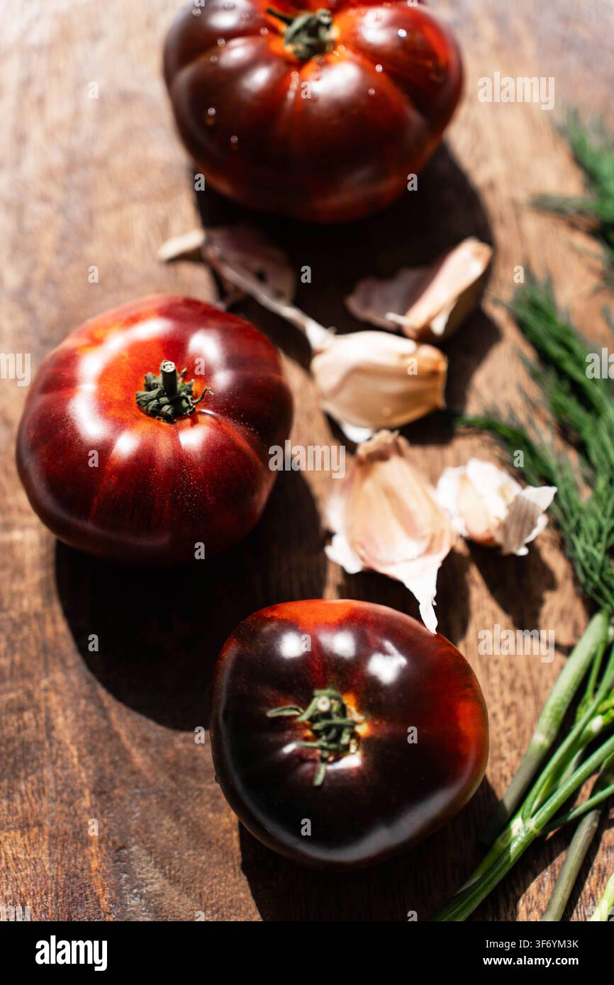 Dunkle Heirloom-Tomaten mit Knoblauch und frischem Dill auf einem rustikalen Holzbrett. Oberansicht Stockfoto