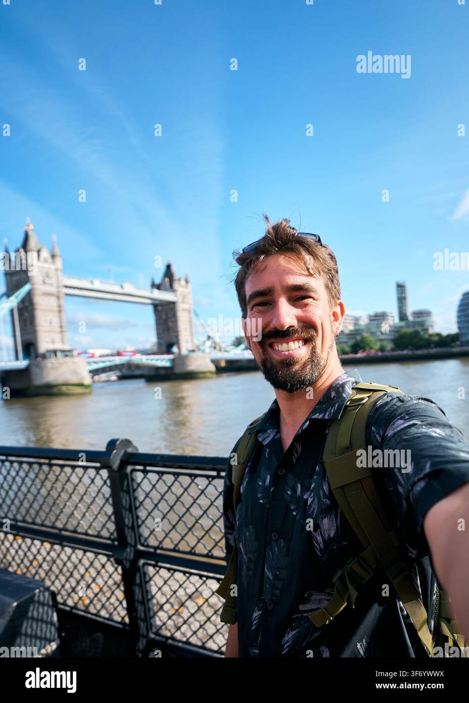 Lächelnder männlicher Tourist, der ein Selfie mit der Tower Bridge macht, während er in London Sightseeing macht Stockfoto