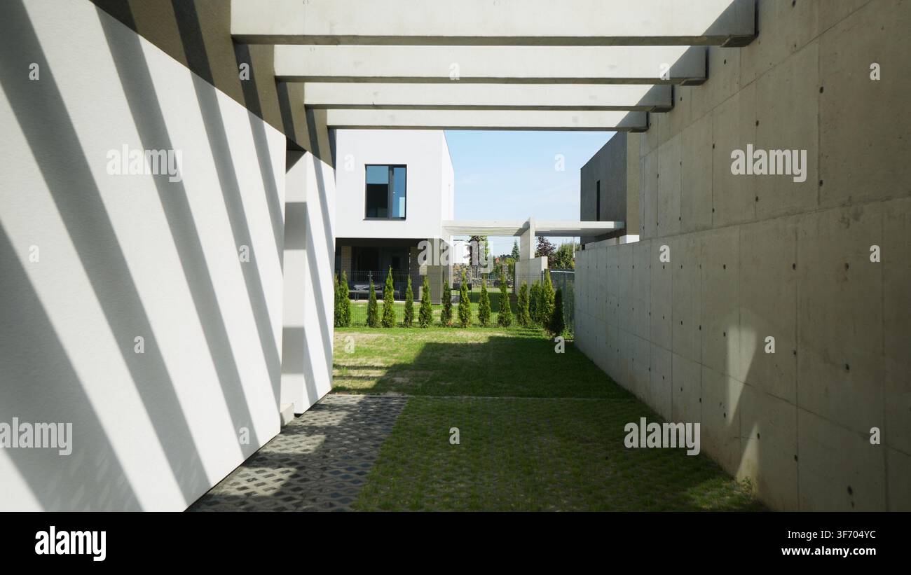 Modernes Haus, das Architektur und Schattenmuster an einer Betonwand mit grünem Rasen im Hinterhof und minimalistischem Design erzeugt Stockfoto