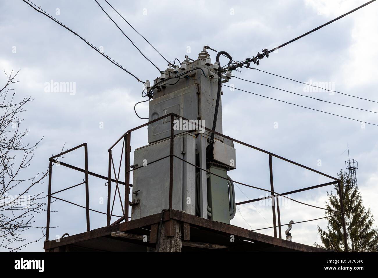 Metallische Stromtransformatoreinheit steht auf einer erhöhten Außenkonstruktion, die mit Freileitungen verbunden ist, und veranschaulicht die Energieversorgung, Elektroingenieur Stockfoto