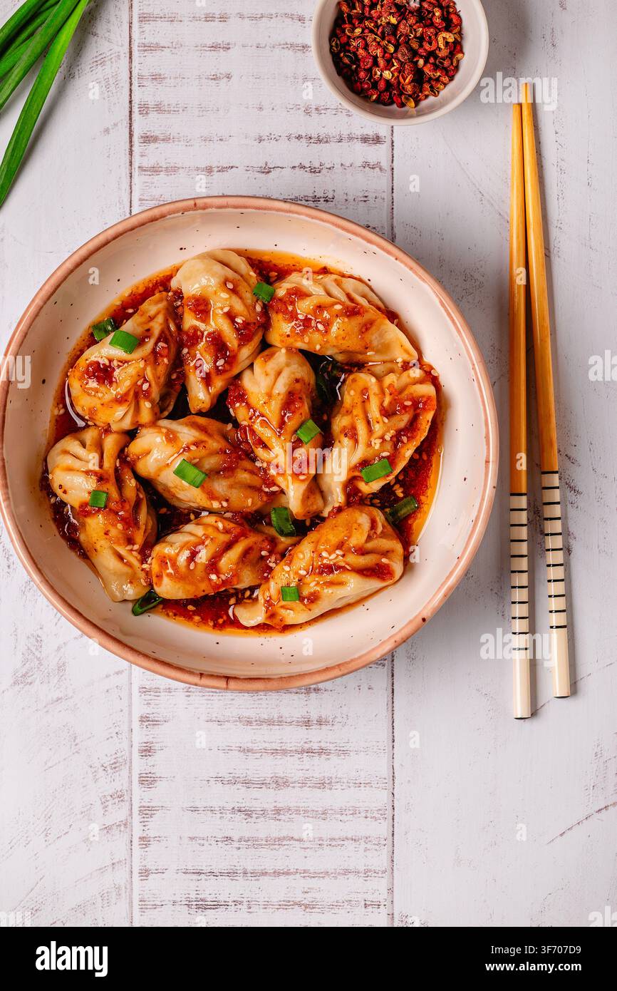 Köstliche Knödel serviert in einer Schüssel mit einer scharfen Soße und grünen Zwiebeln auf einem Holztisch Stockfoto