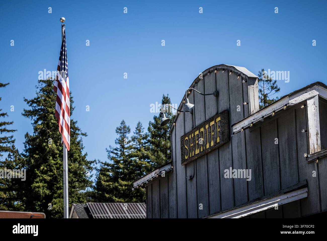 Rustikales hölzernes Sheriff-Bürogebäude und amerikanische Flagge, die hoch weht Stockfoto