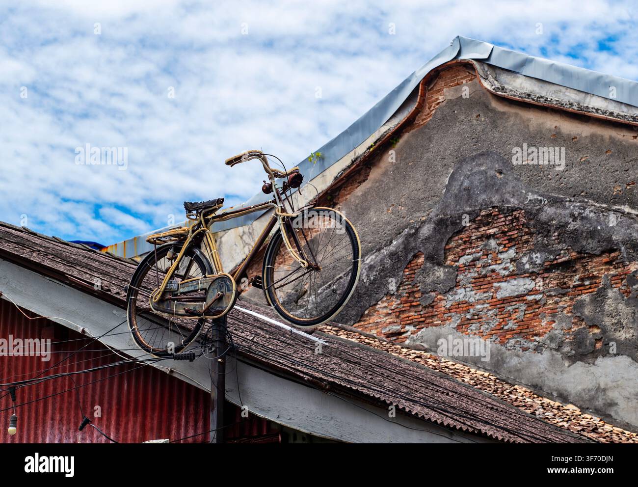 Vintage-Fahrrad montiert über der Dachkante vor einer rustikalen Ziegelmauer Stockfoto
