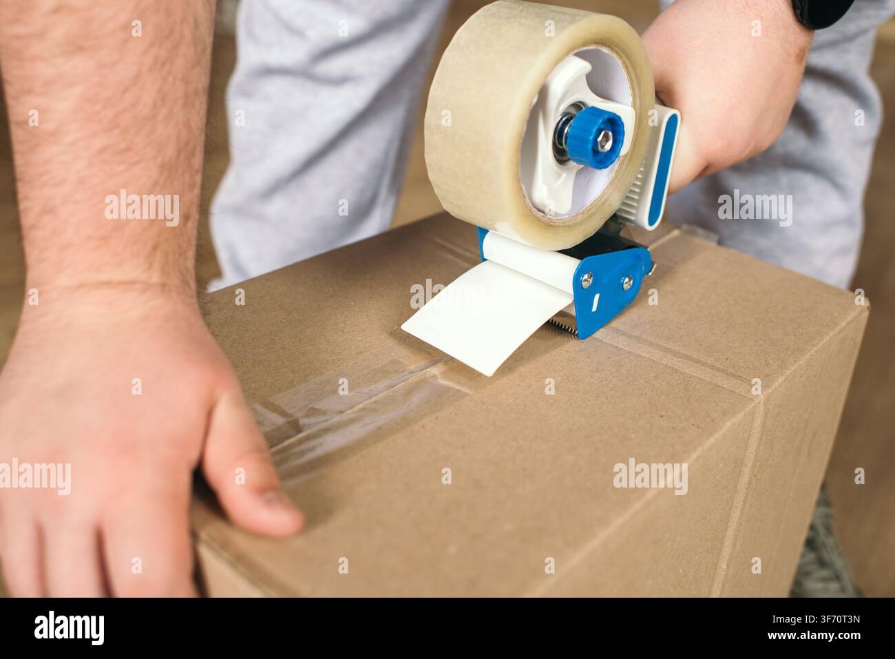 Nahaufnahme eines Arbeiters, der einen Karton mit einem Klebebandabroller versiegelt Stockfoto