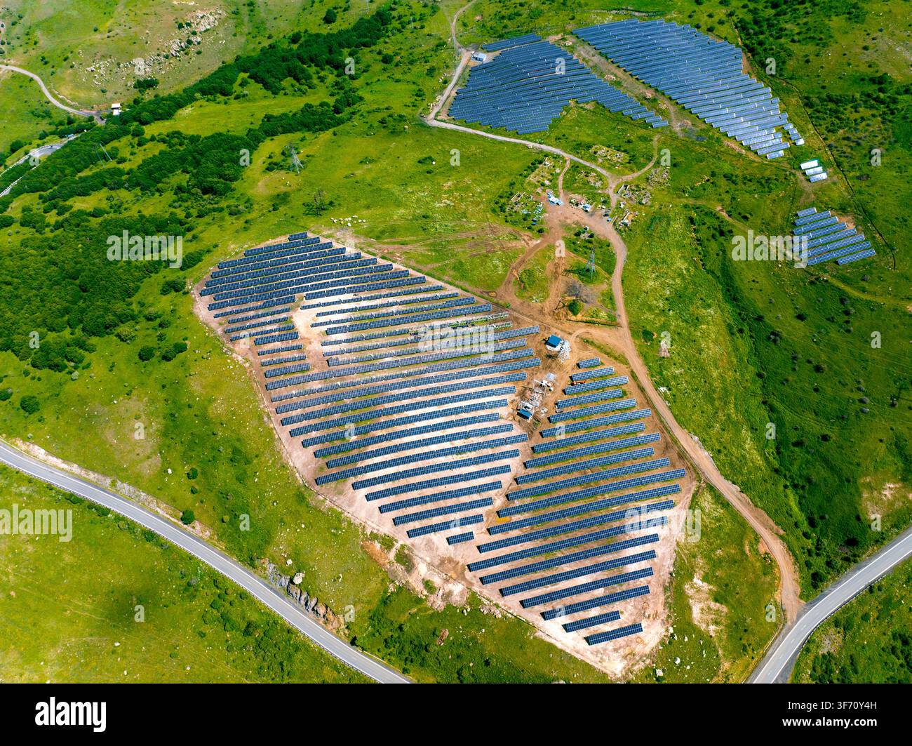 Luftbild von Solarpanelen, die auf grünen Hügeln installiert sind. Die Paneele sind in ordentlichen Reihen über das hügelige Gelände angeordnet. Straßen winden sich um die Anlagen Stockfoto