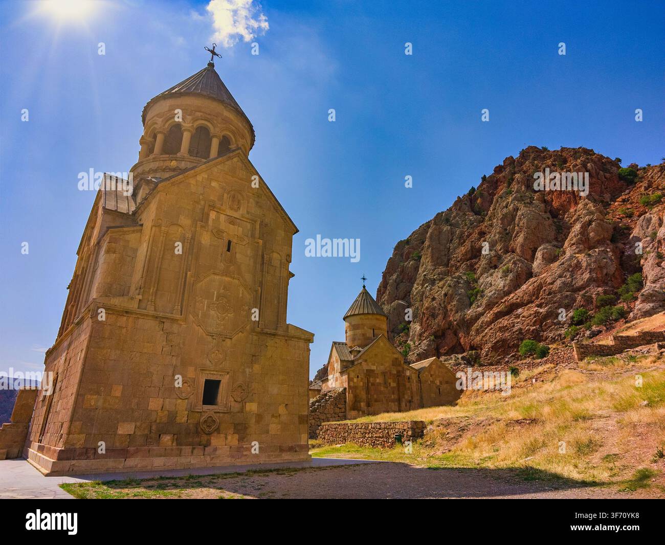 Alte steinerne Noravank-Kirche unter strahlend blauem Himmel. Eine felsige Klippe umgibt die Struktur. Sonnenlicht hebt architektonische Details hervor Stockfoto