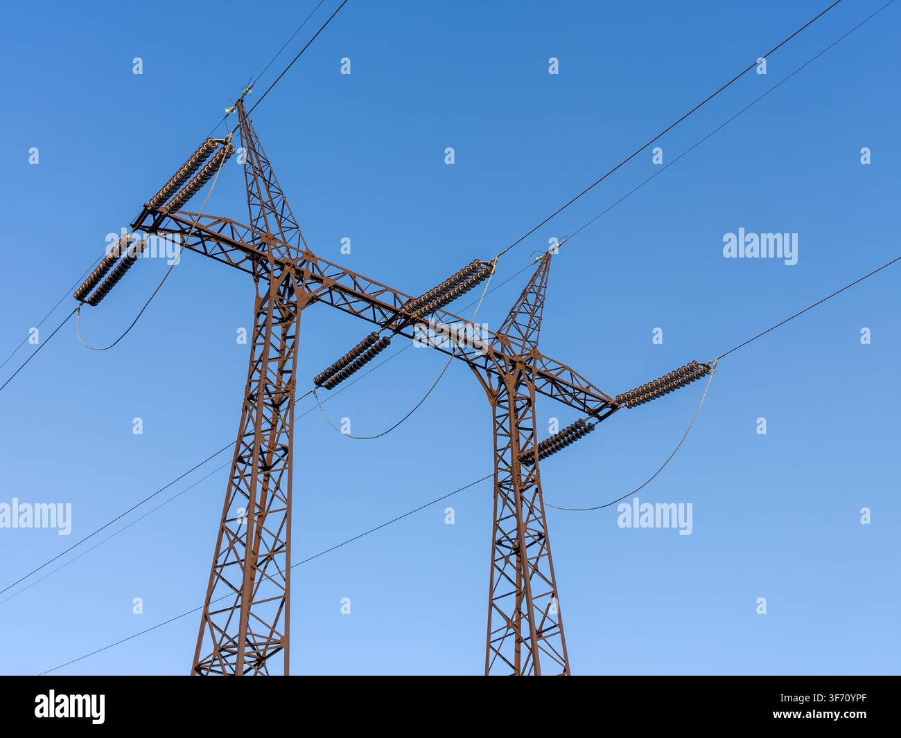 Zwei hohe Metall-Hochspannungsmasten vor einem klaren blauen Himmel. Drähte spannen sich zwischen den Konstruktionen Stockfoto