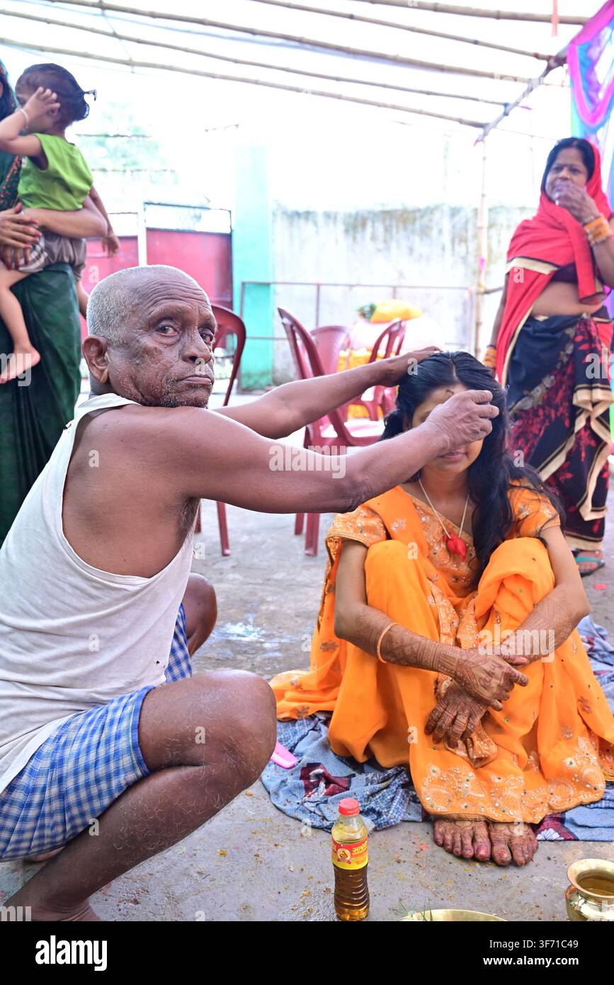 Alter indischer Mann führt das Sindoor-Ritual an einer jungen bengalischen Braut in gelbem Saree während der hinduistischen Hochzeitszeremonie im Dorf durch Stockfoto