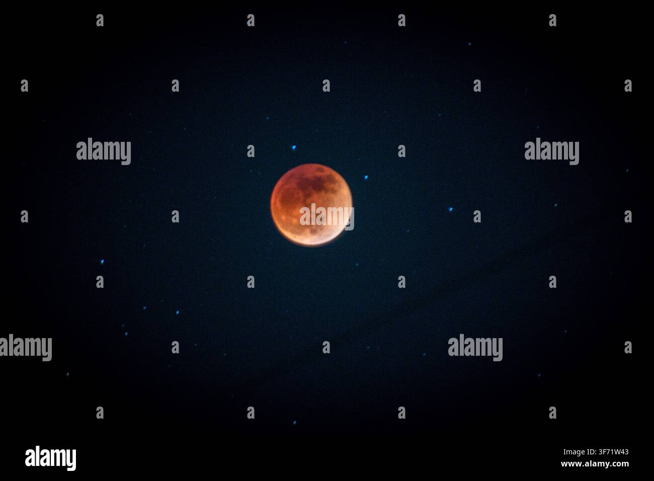Ein tiefes orange-rotes Blutmond leuchtet während einer totalen Mondfinsternis, umgeben von schwachen Sternen in einem dunklen Nachthimmel. Stockfoto