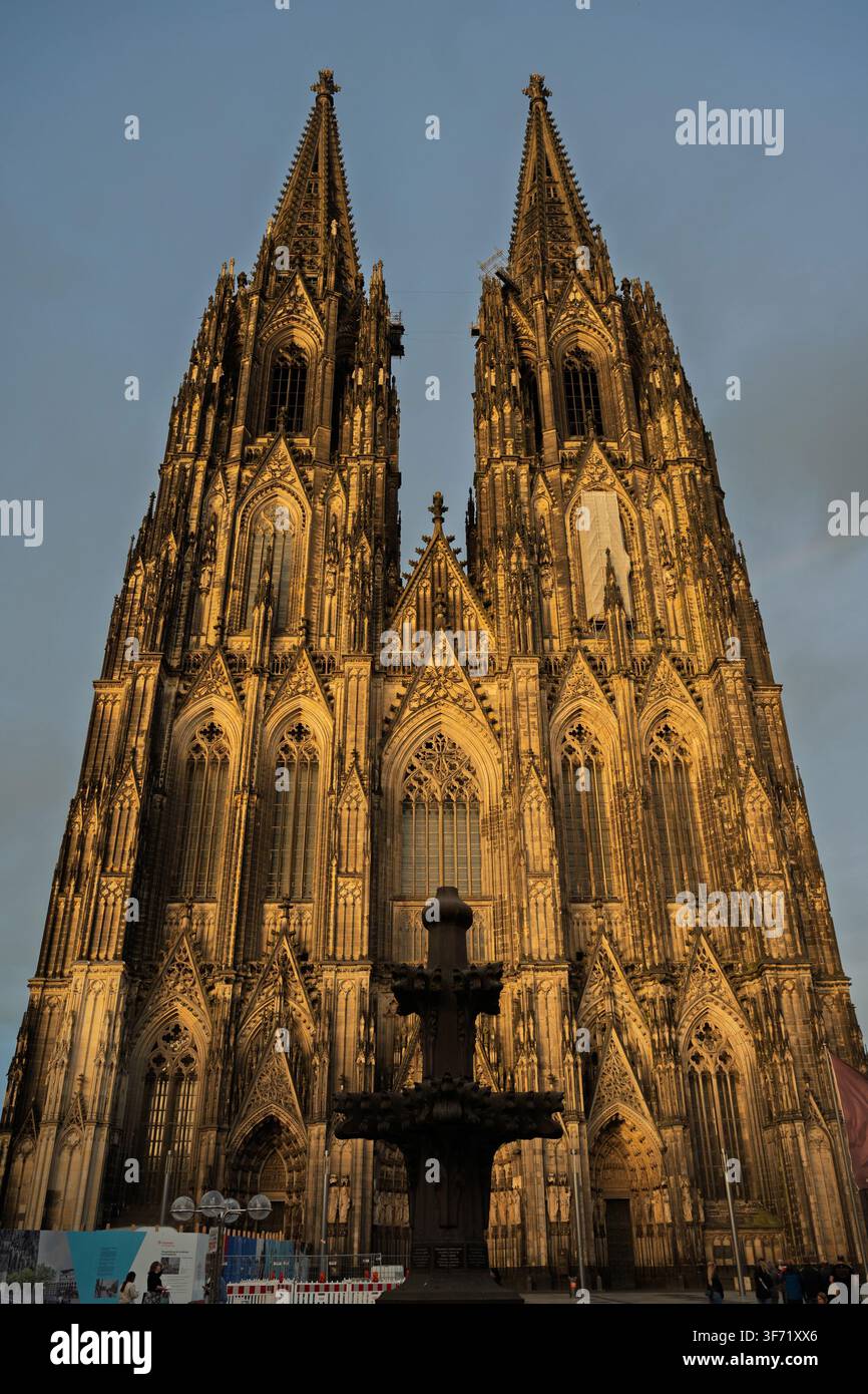 Die kunstvolle gotische Fassade und die beiden Türme des Kölner Domes leuchten im warmen Abendlicht vor einem dramatischen Himmel. Stockfoto