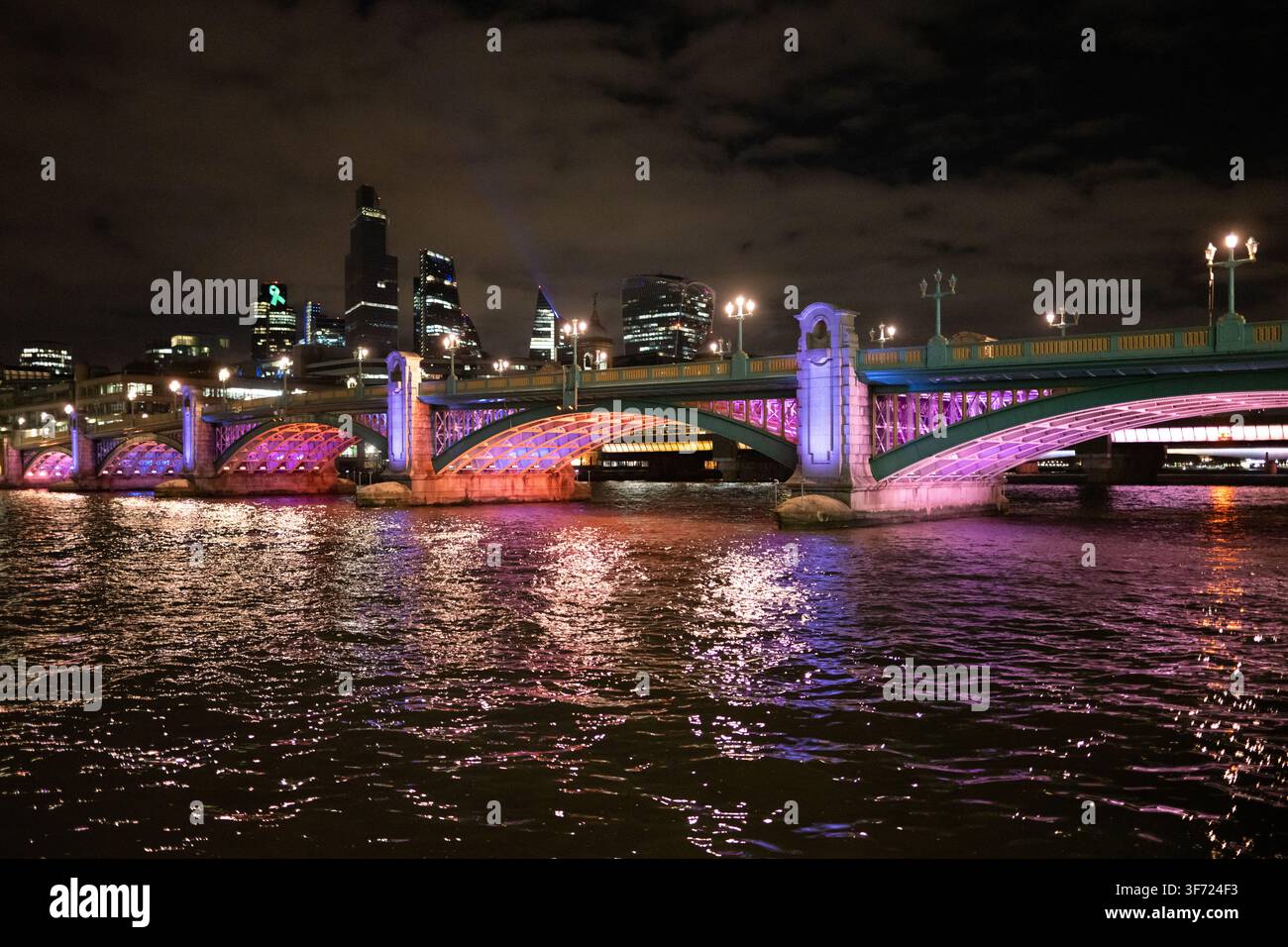 Die Londoner Blackfriars Bridge leuchtet im Rahmen des Leuchtturmprojekts lila und spiegelt sich in der berühmten Skyline der Stadt wider. Stockfoto