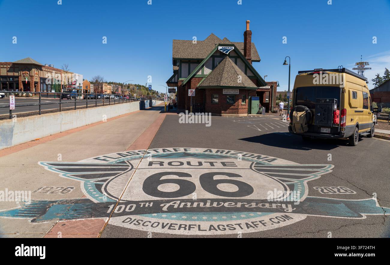Ein zum 100. Jubiläum der Route 66 auf den Bürgersteig gemaltes Schild in der Nähe des historischen Amtrak-Besucherzentrums mit einem geparkten Van in Flagstaff, Arizona Stockfoto