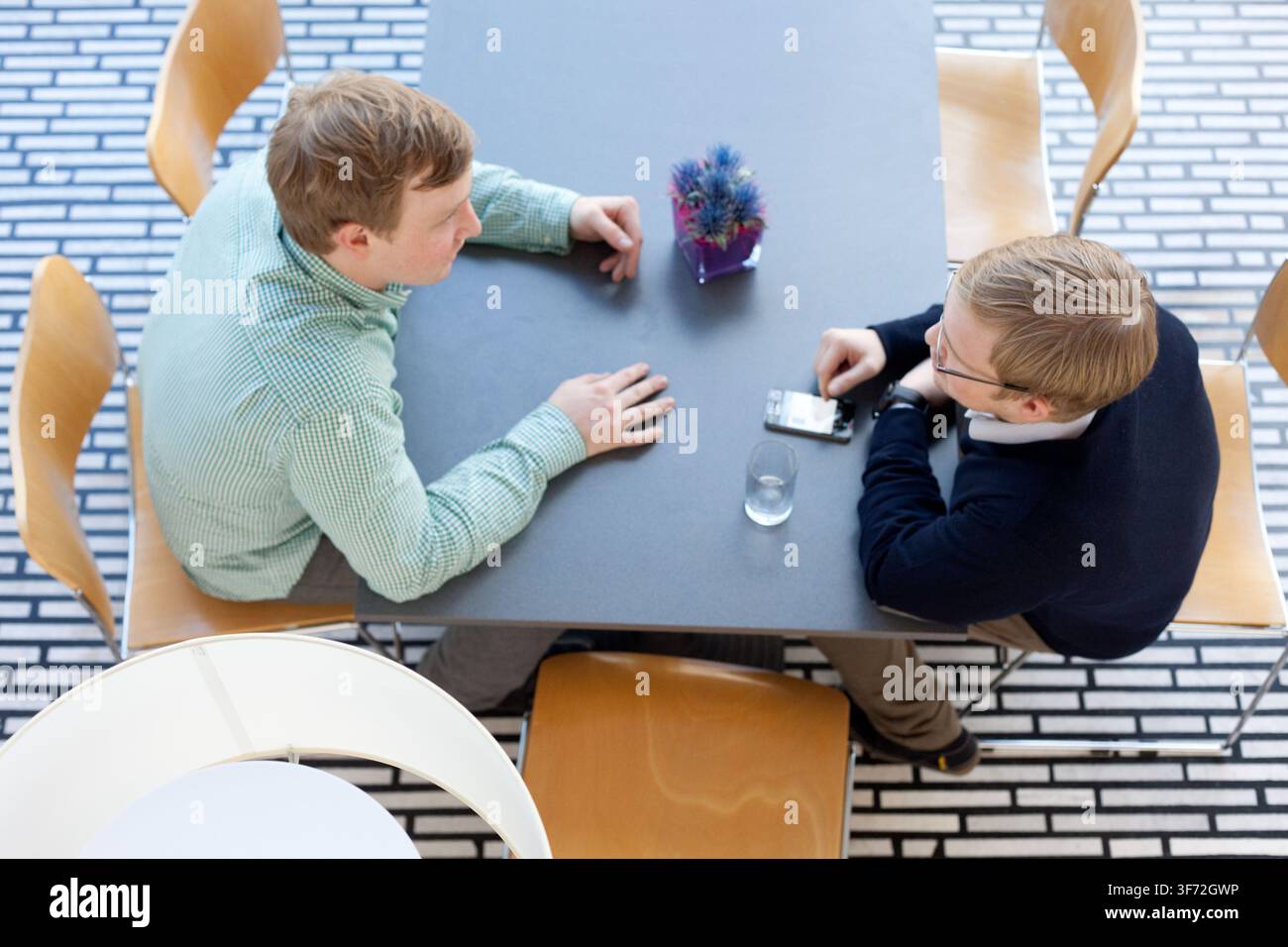 Zwei Männer diskutieren ein Gerät an einem Tisch im Guggenheim Museum Bilbao und verbinden professionelle Gespräche mit einer modernen Wahrzeichen-Umgebung. Stockfoto