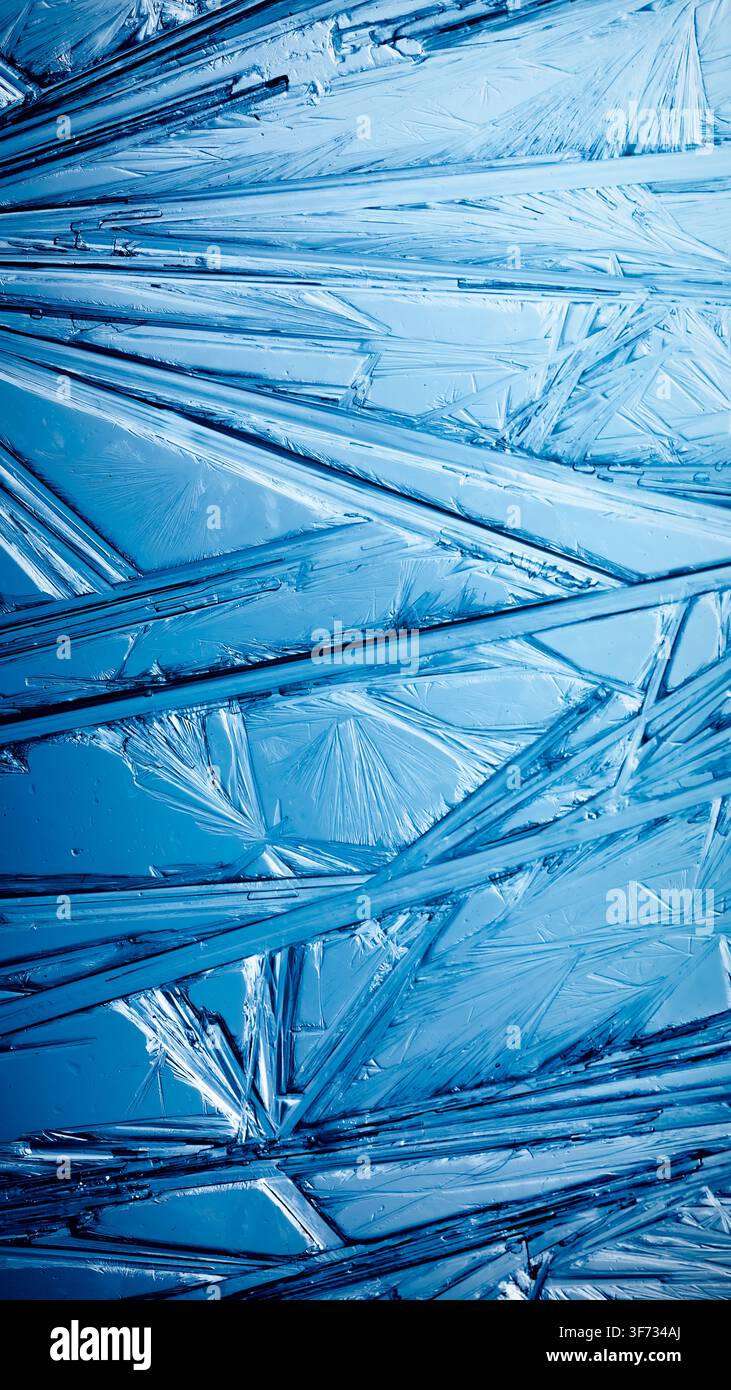 Eis, das in kunstvollen Mustern aus zarten Kristallen mit brillanten Kontrastierungen von tiefem Blau gefroren ist. Echte einzigartige kristalline Formationen. Funkelnder Wind Stockfoto